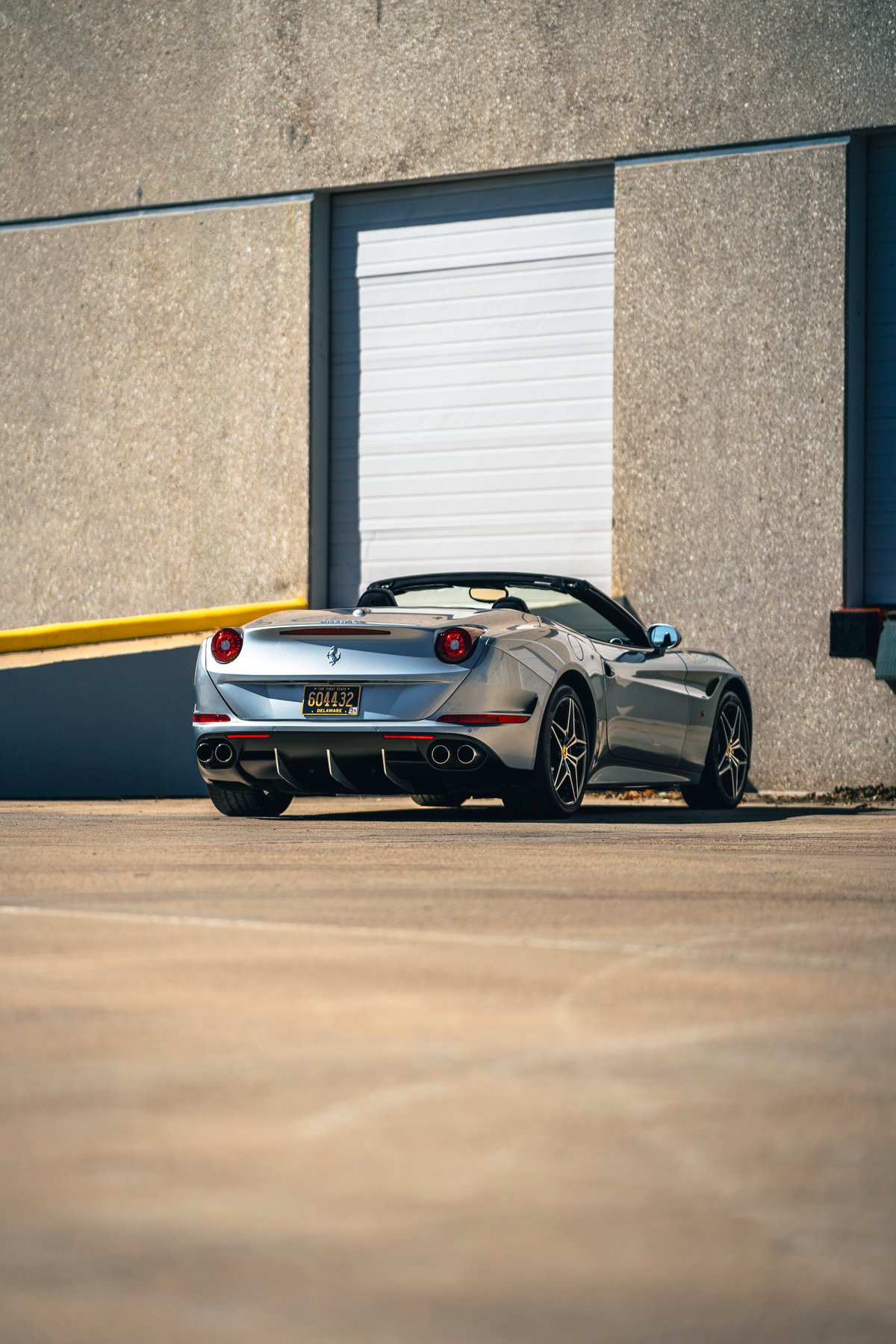 Rear view of a silver 2016 Ferrari California T convertible with black rims.