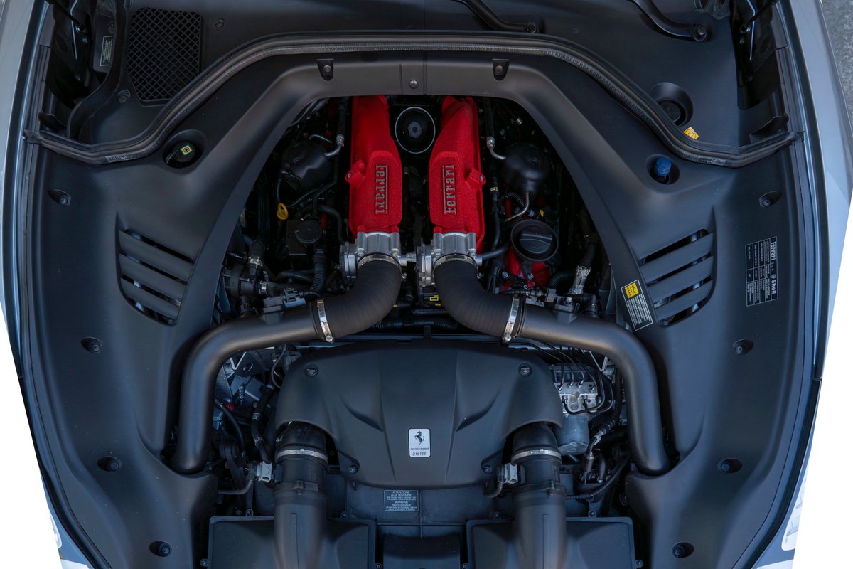 Overhead view of a 2016 Ferrari California T engine bay, showing red Ferrari engine covers and black intake tubes.