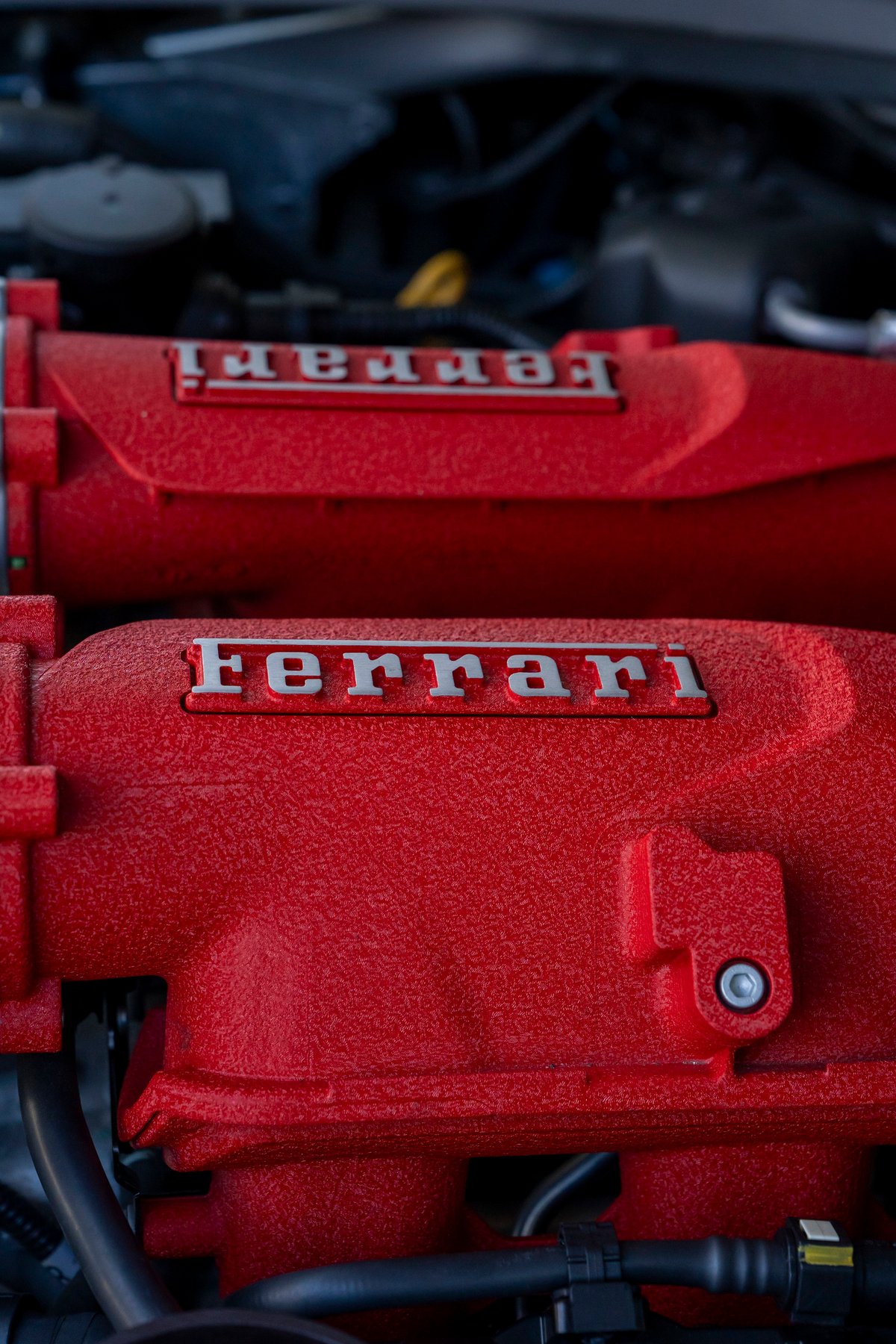 Close-up of a red Ferrari engine intake manifold with silver "Ferrari" badging.