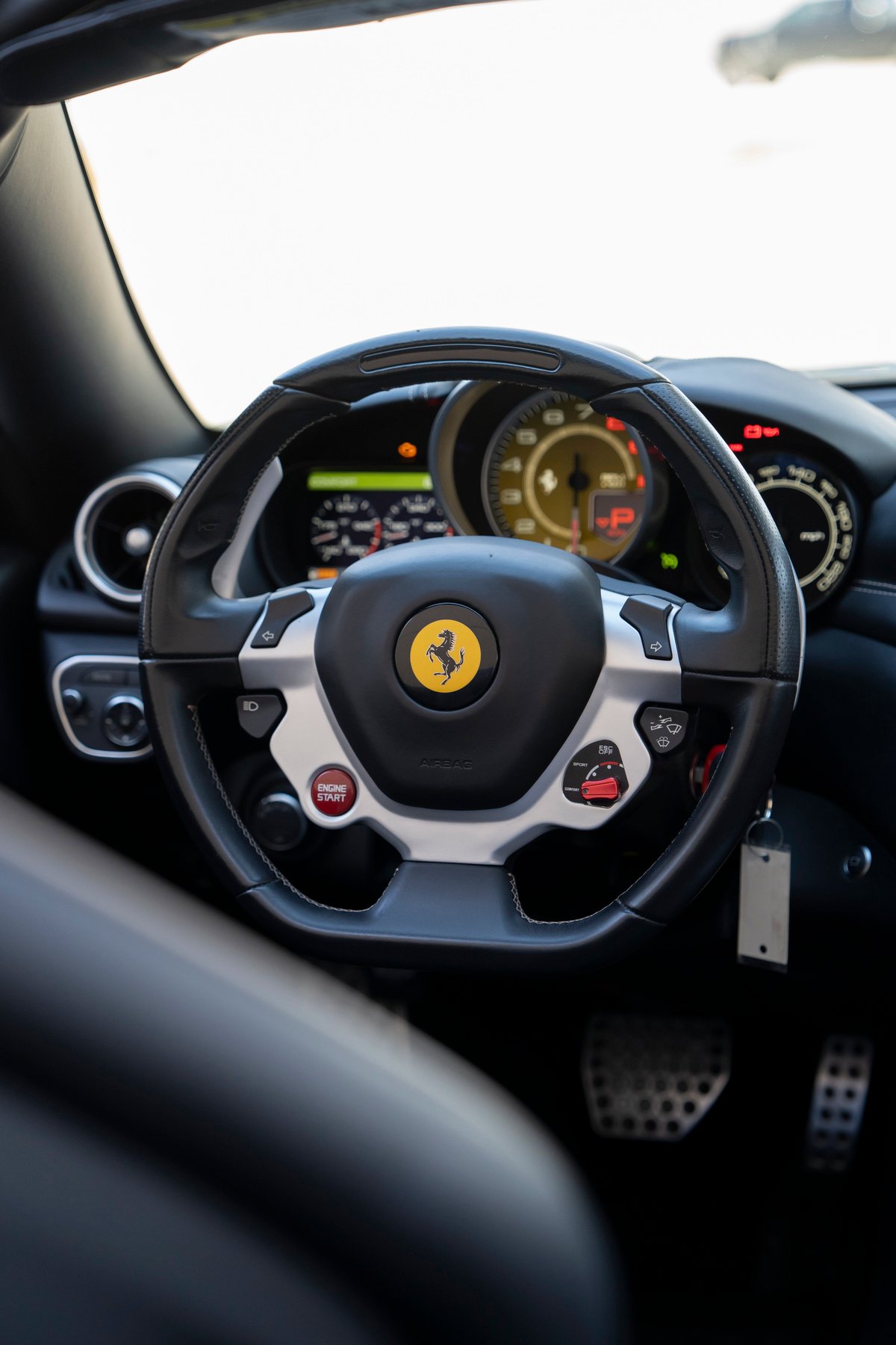 Black leather steering wheel with silver trim and red engine start button in a 2016 Ferrari California T.