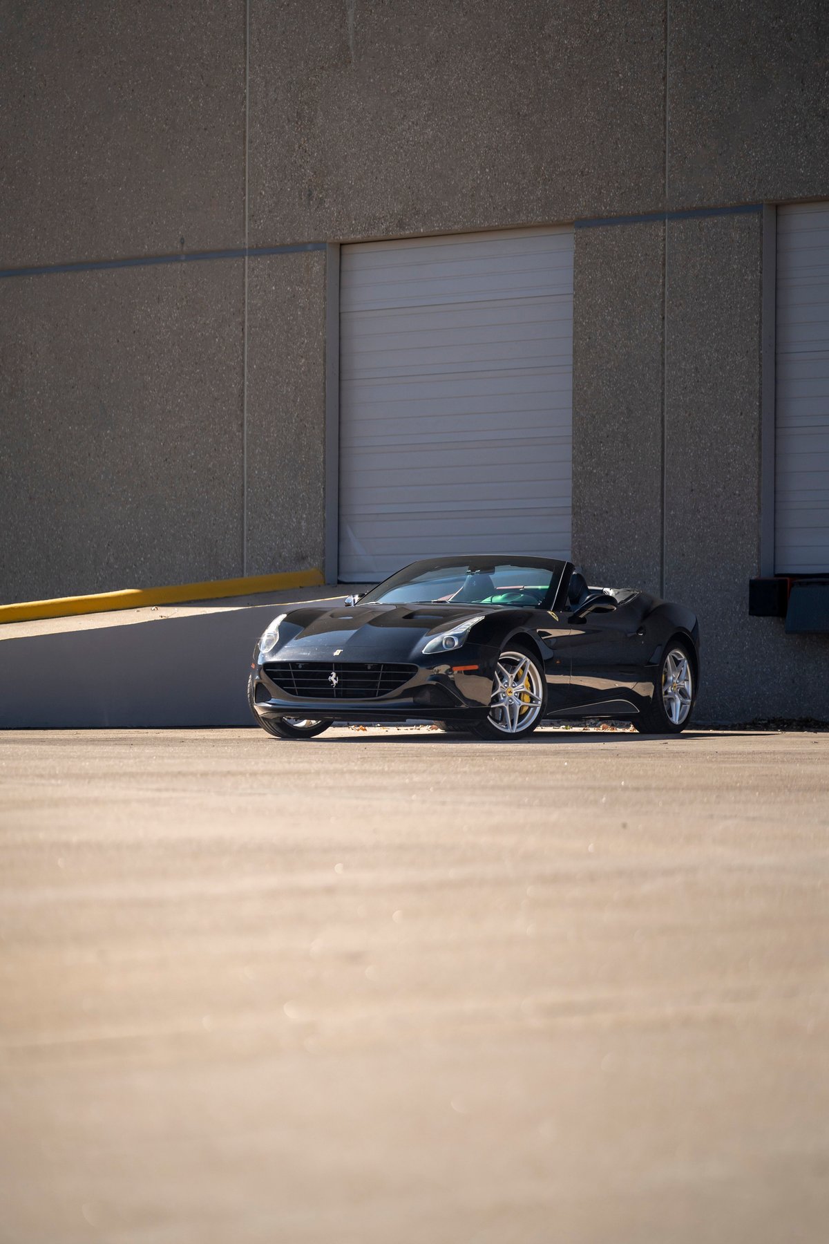 Black 2016 Ferrari California T convertible with silver rims parked outdoors.