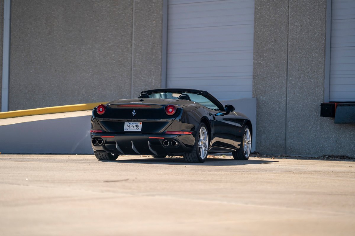 Black 2016 Ferrari California T convertible with silver rims, quad exhaust, and red trim.