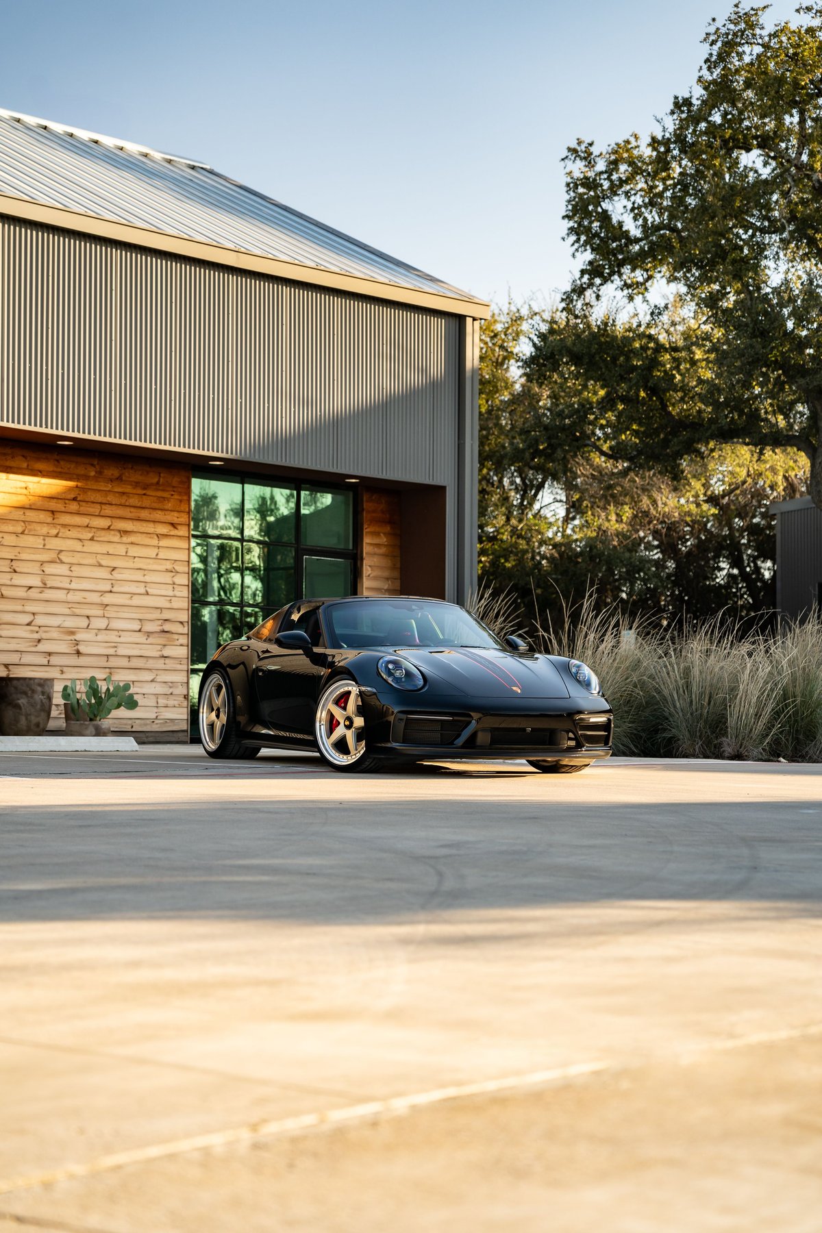 Black 2023 Porsche 911 Carrera 4 GTS with red stripe livery and custom gold rims.