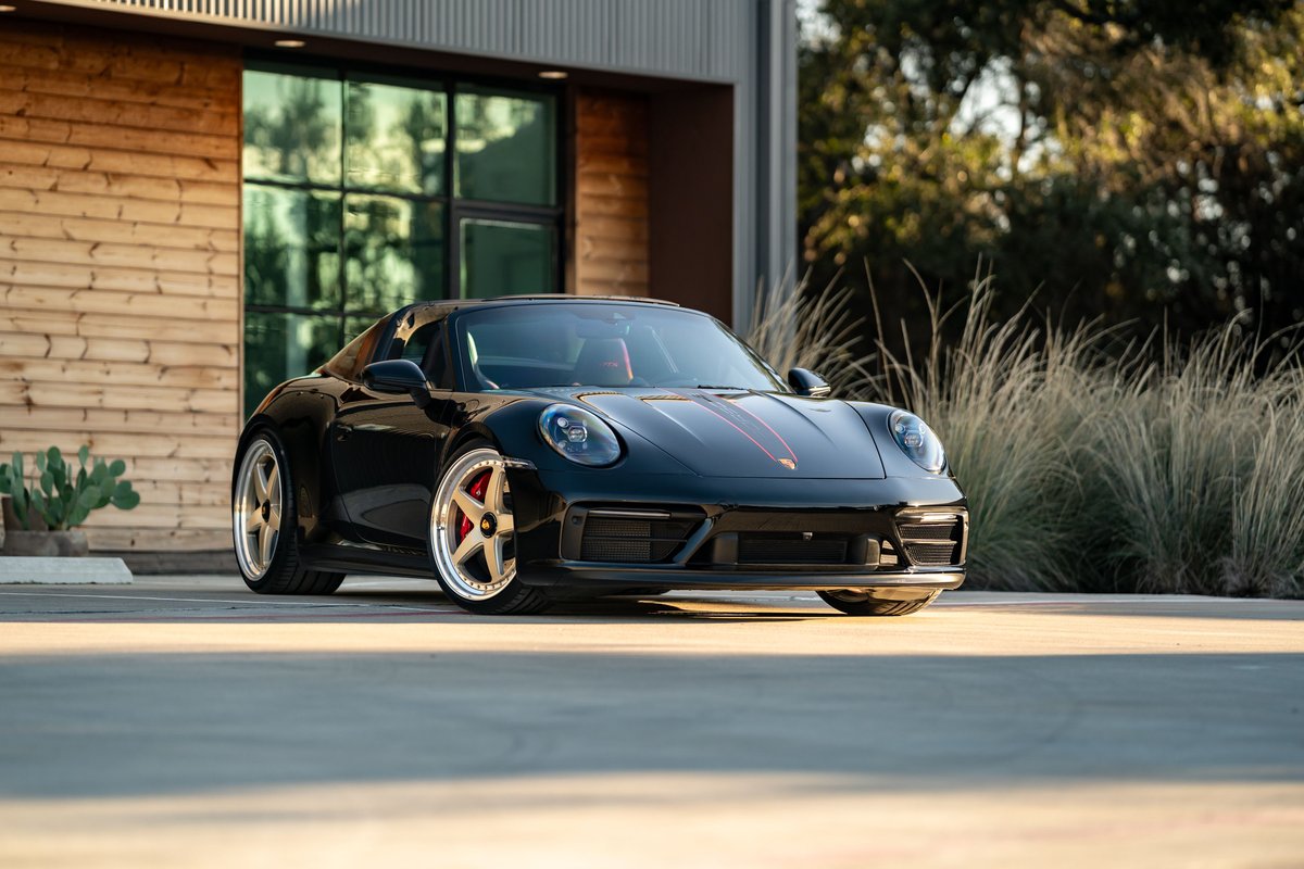 Black 2023 Porsche 911 Carrera 4 GTS with red stripe livery and polished rims.