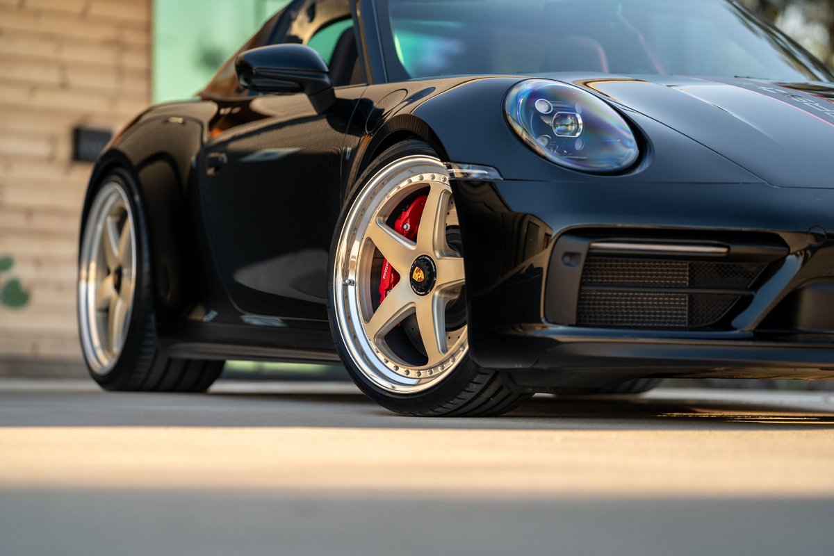 Black 2023 Porsche 911 Carrera 4 GTS with gold multi-spoke rims and red brake calipers.