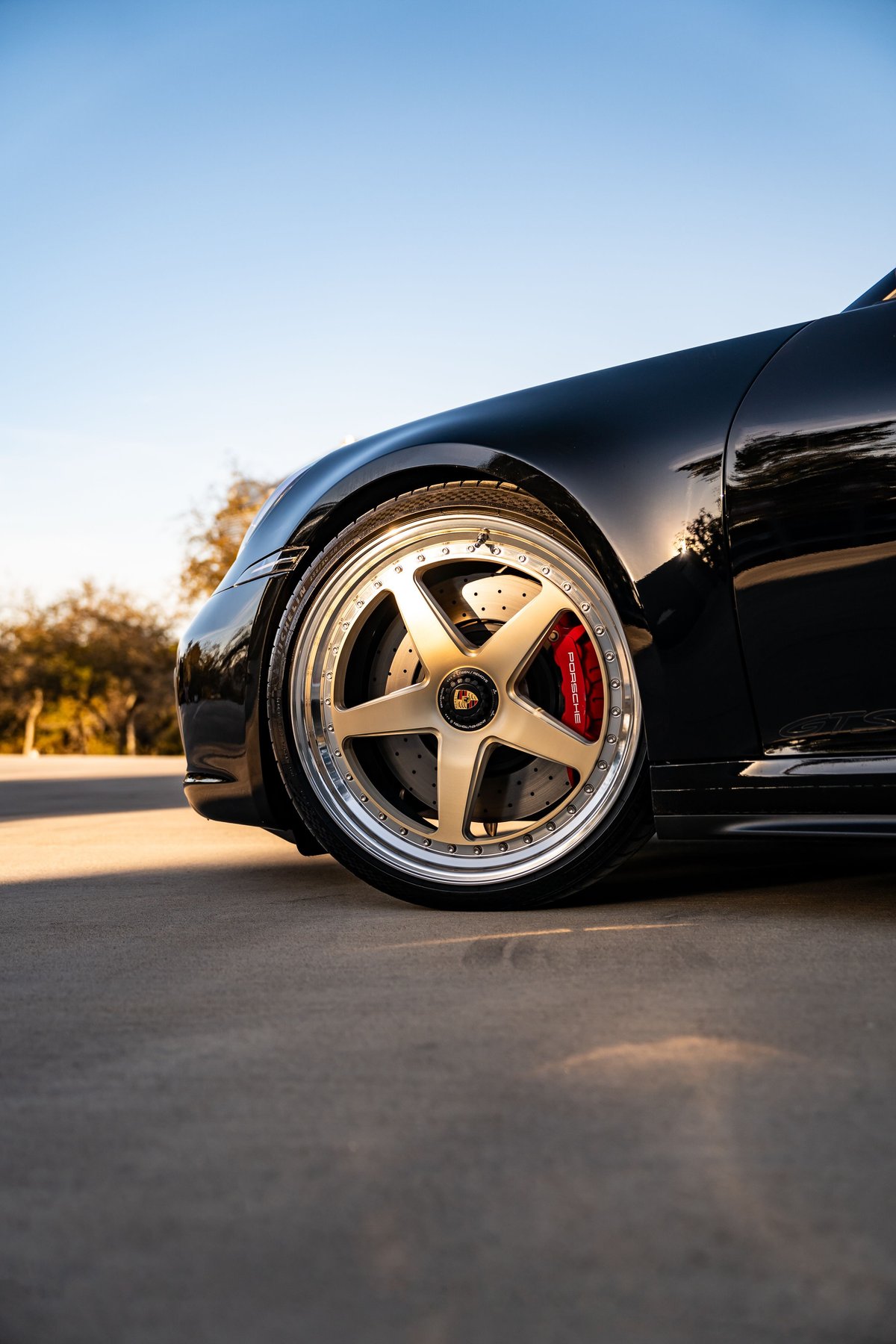 Black 2023 Porsche 911 Carrera 4 GTS with gold five-spoke rims and red brake calipers.