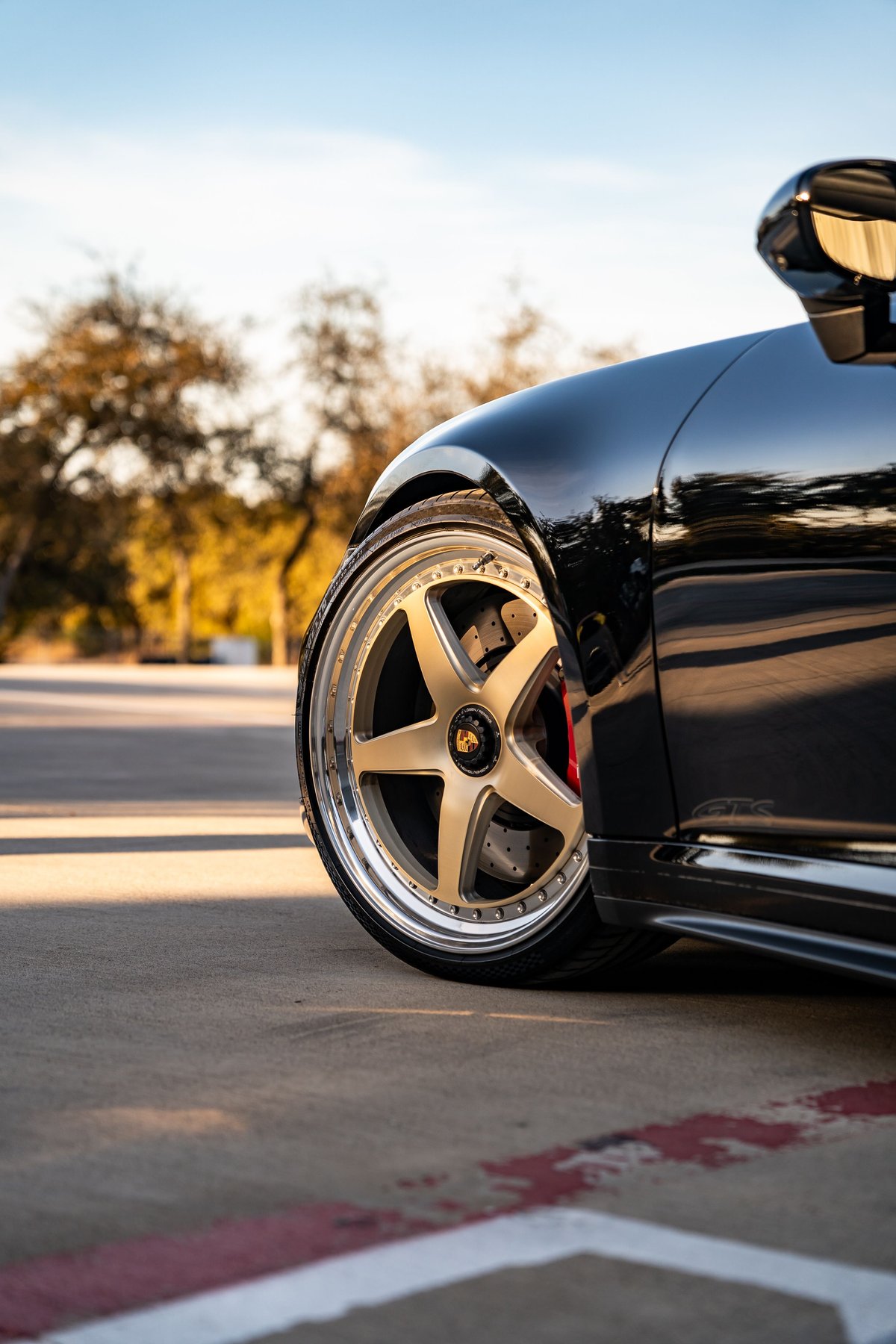 Close up of a black 2023 Porsche 911 Carrera 4 GTS wheel with gold multi-spoke rims.