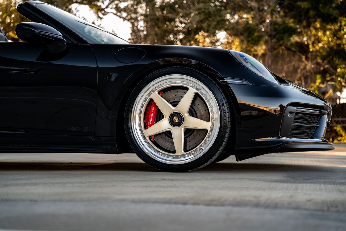 Close-up of a black 2023 Porsche 911 Carrera 4 GTS with gold five-spoke rims and red brake calipers.