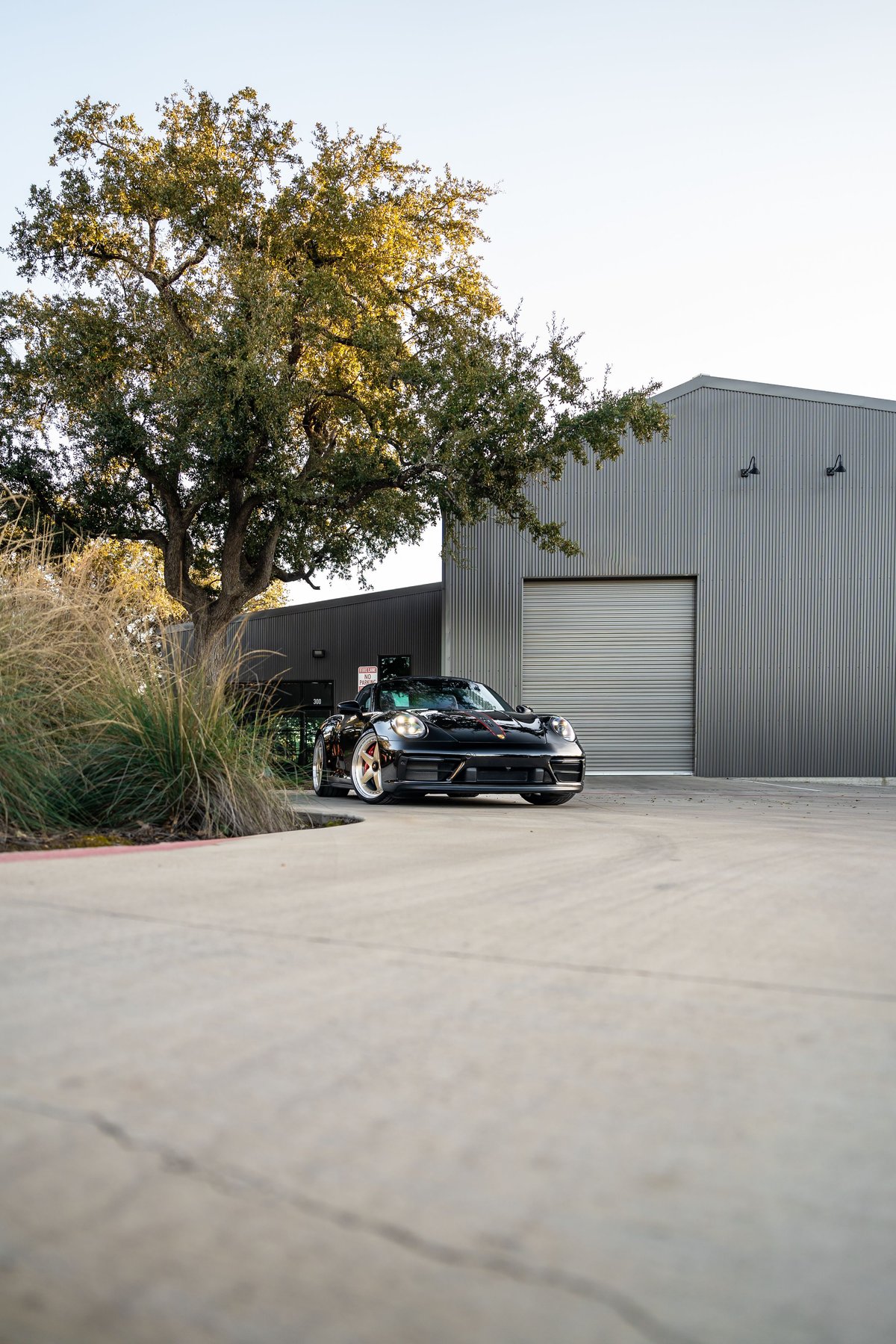 Black 2023 Porsche 911 Carrera 4 GTS with gold rims parked outside a modern building.