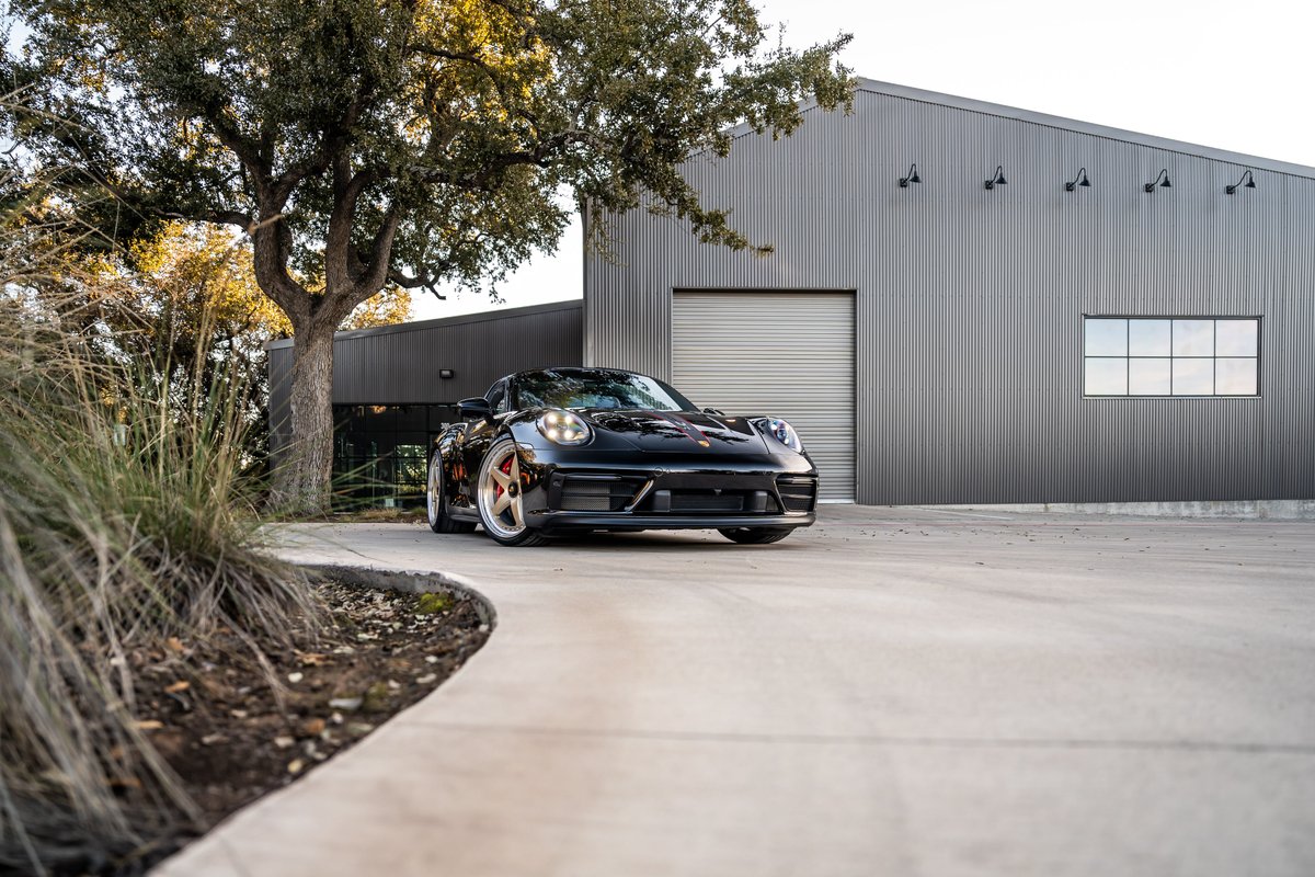 Black 2023 Porsche 911 Carrera 4 GTS with striking copper rims, parked in front of a modern warehouse.
