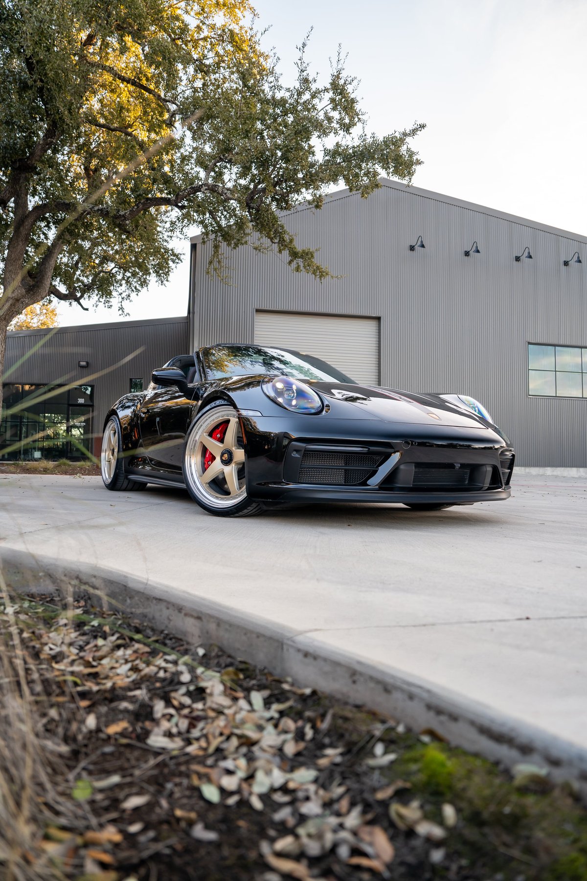 Black 2023 Porsche 911 Carrera 4 GTS convertible with gold rims and red brake calipers.
