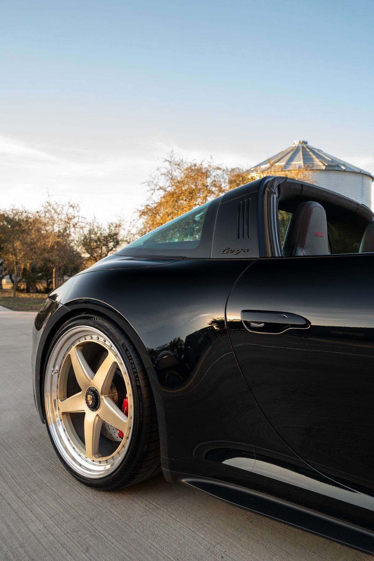 Black 2023 Porsche 911 Carrera 4 GTS Targa with gold five-spoke rims and red brake calipers.