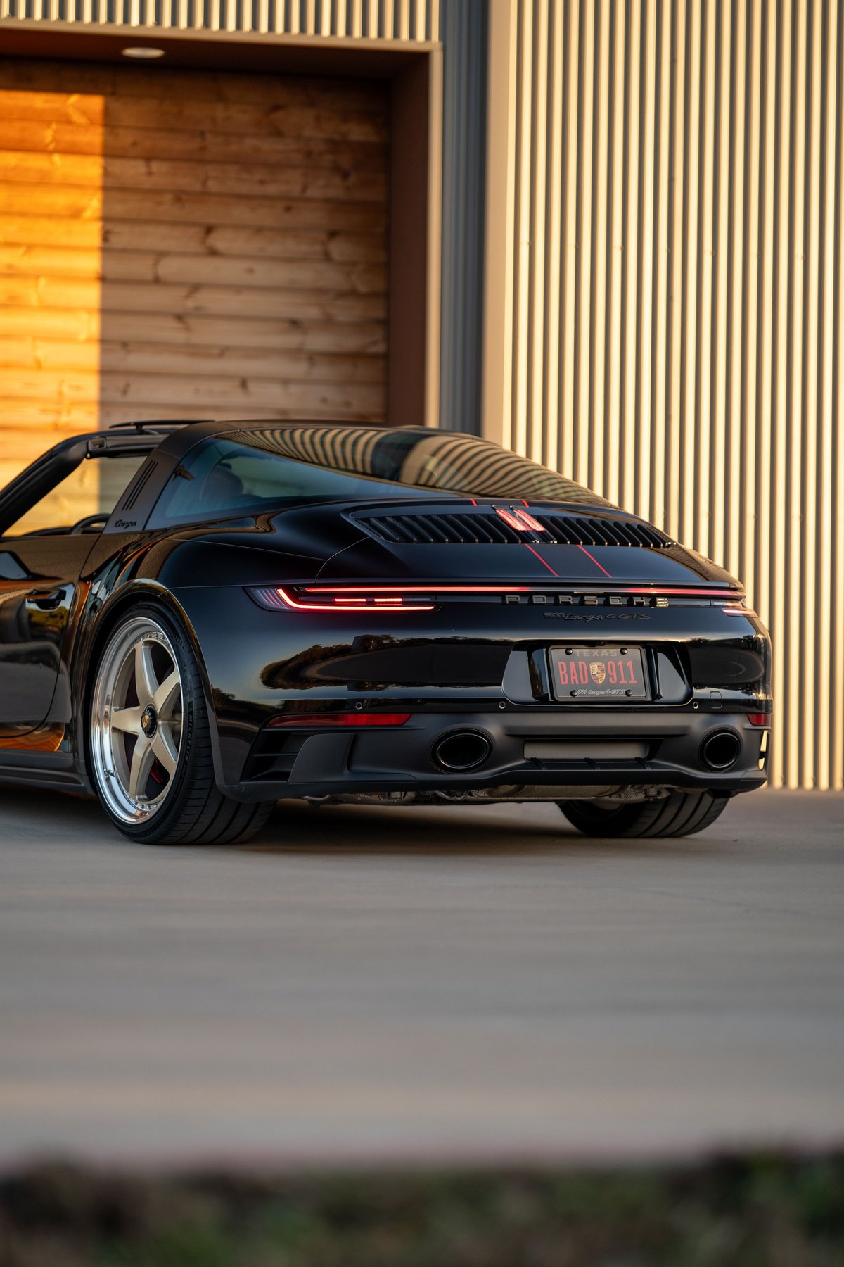 Black 2023 Porsche 911 Carrera 4 GTS Targa with red stripe livery and silver rims.