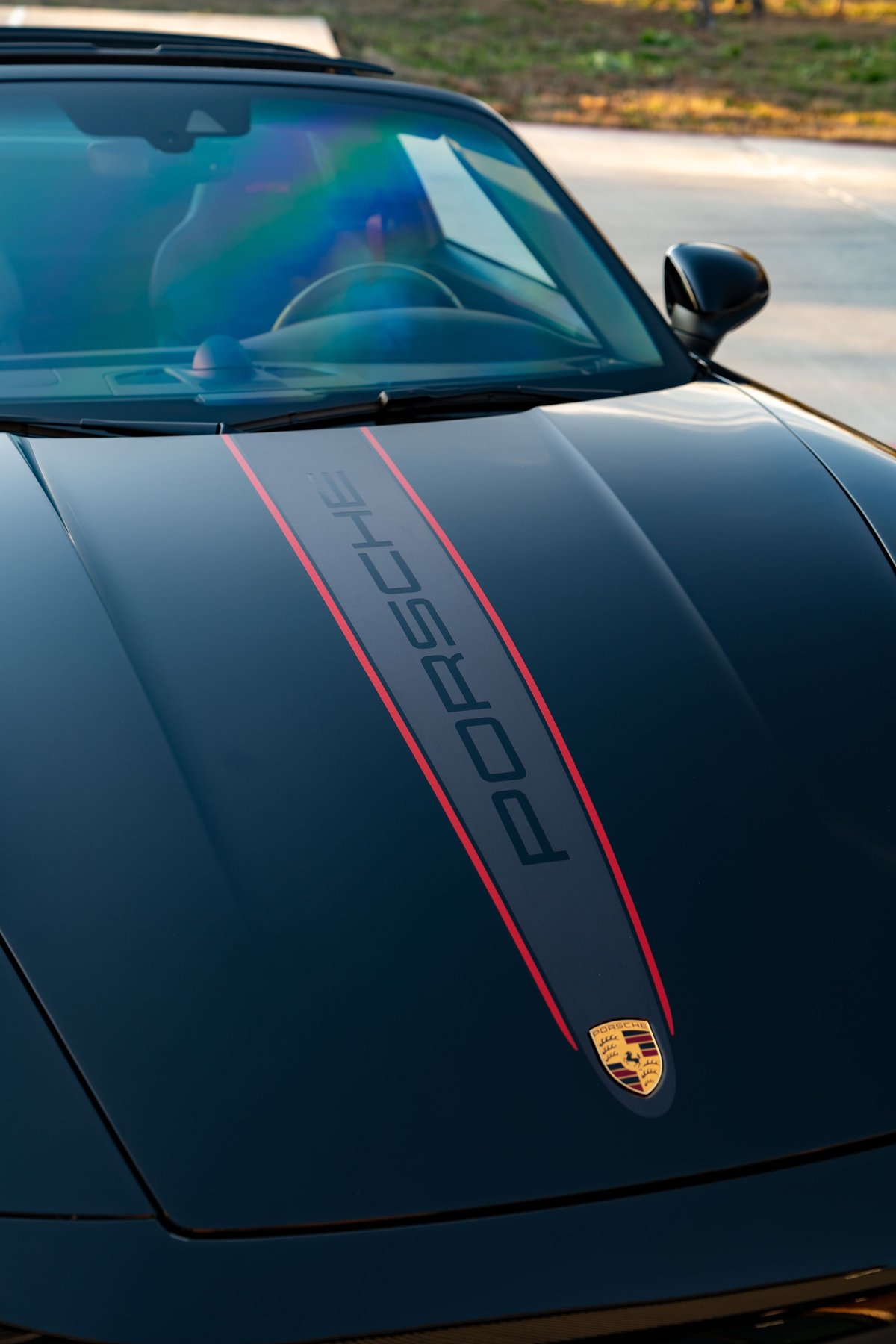 Black 2023 Porsche 911 Carrera 4 GTS hood with central stripe and Porsche crest.