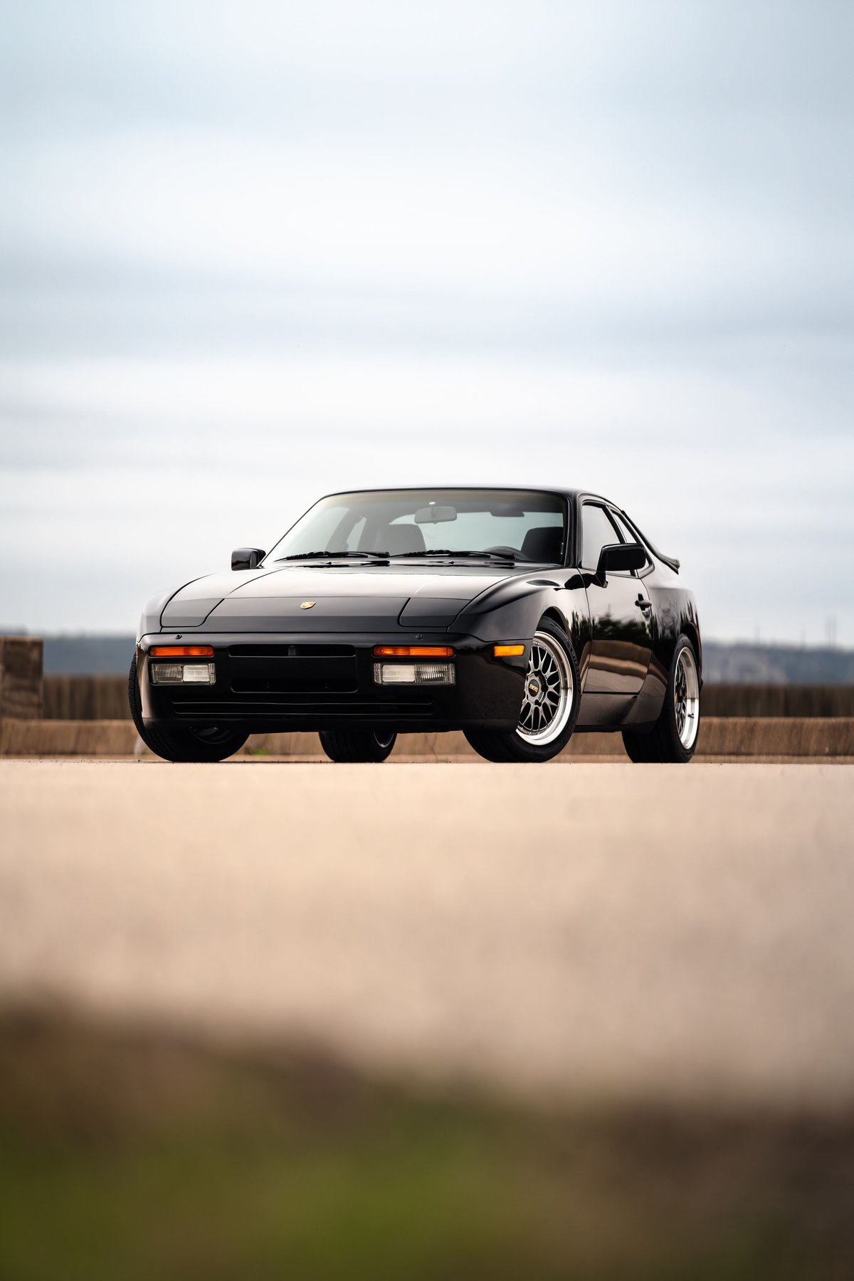 Black 1986 Porsche 944 Turbo with aftermarket rims parked outdoors.