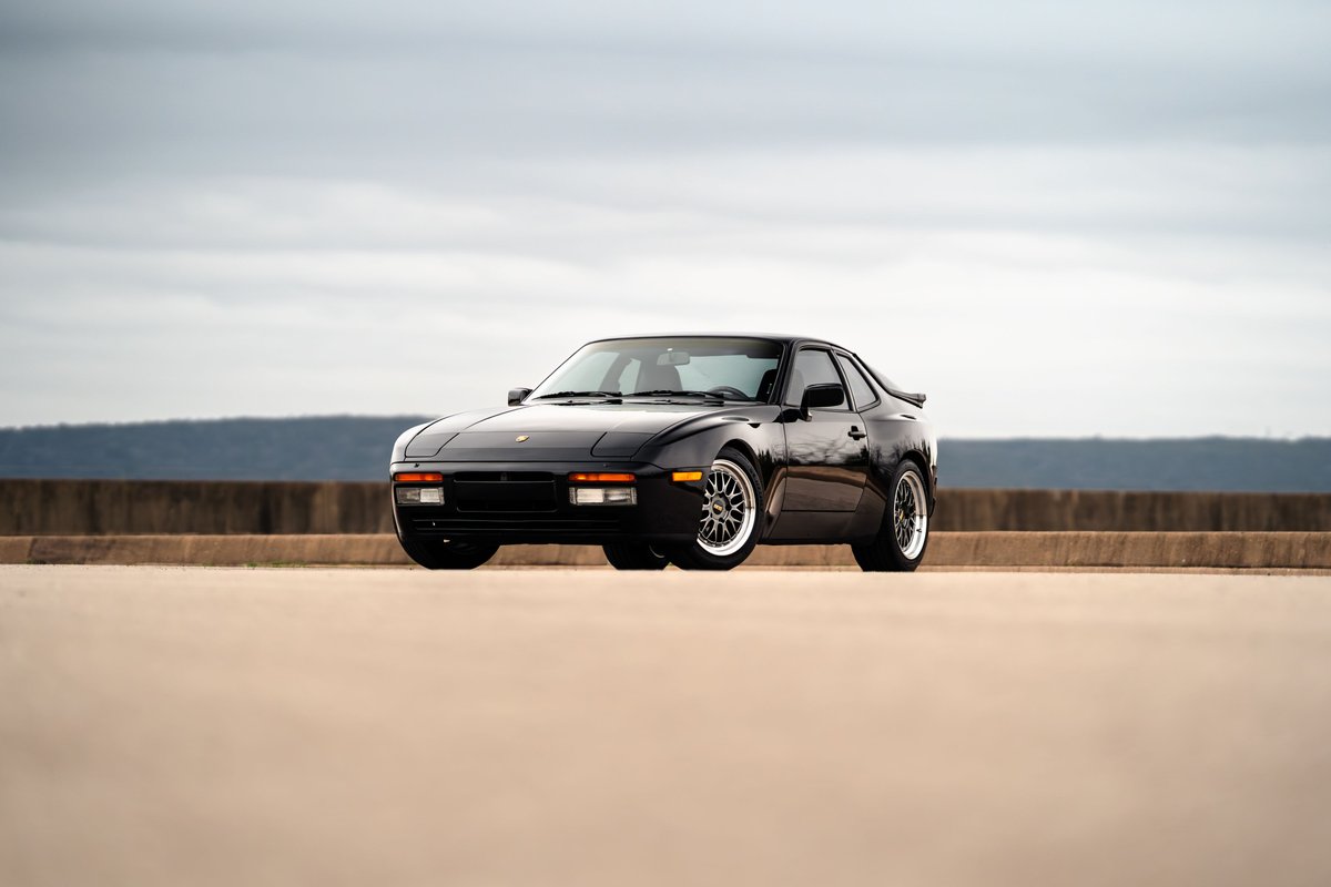 Front 3/4 view of a black 1986 Porsche 944 Turbo with chrome rims.