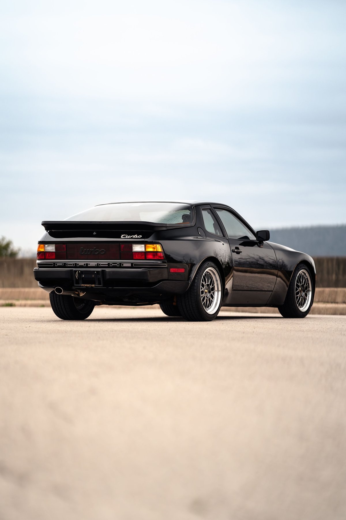 Rear view of a black 1986 Porsche 944 Turbo with chrome mesh rims.