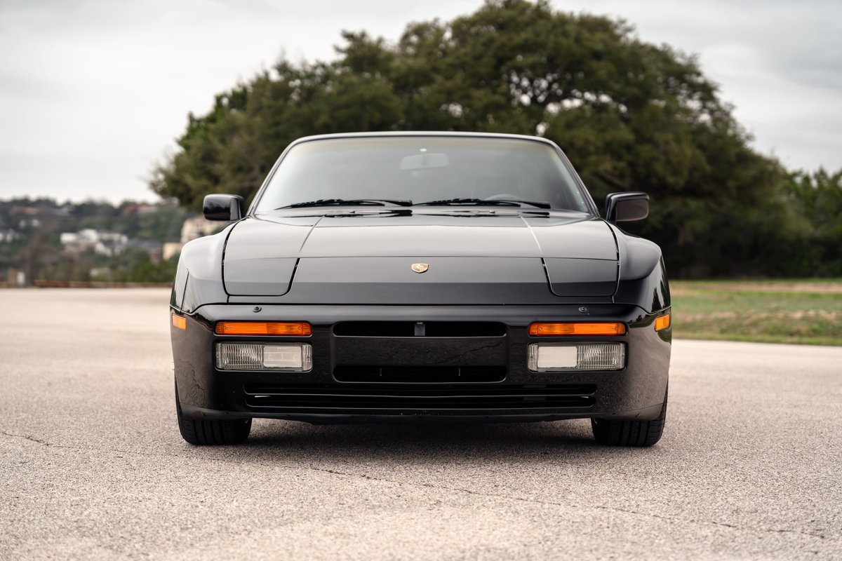 Front view of a black 1986 Porsche 944 Turbo with black trim and pop-up headlights.