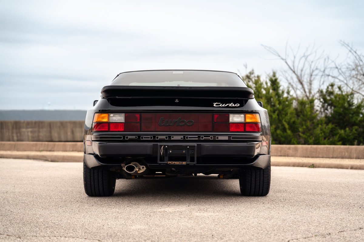Rear view of a black 1986 Porsche 944 Turbo, showcasing its taillights, exhaust, and turbo badging.