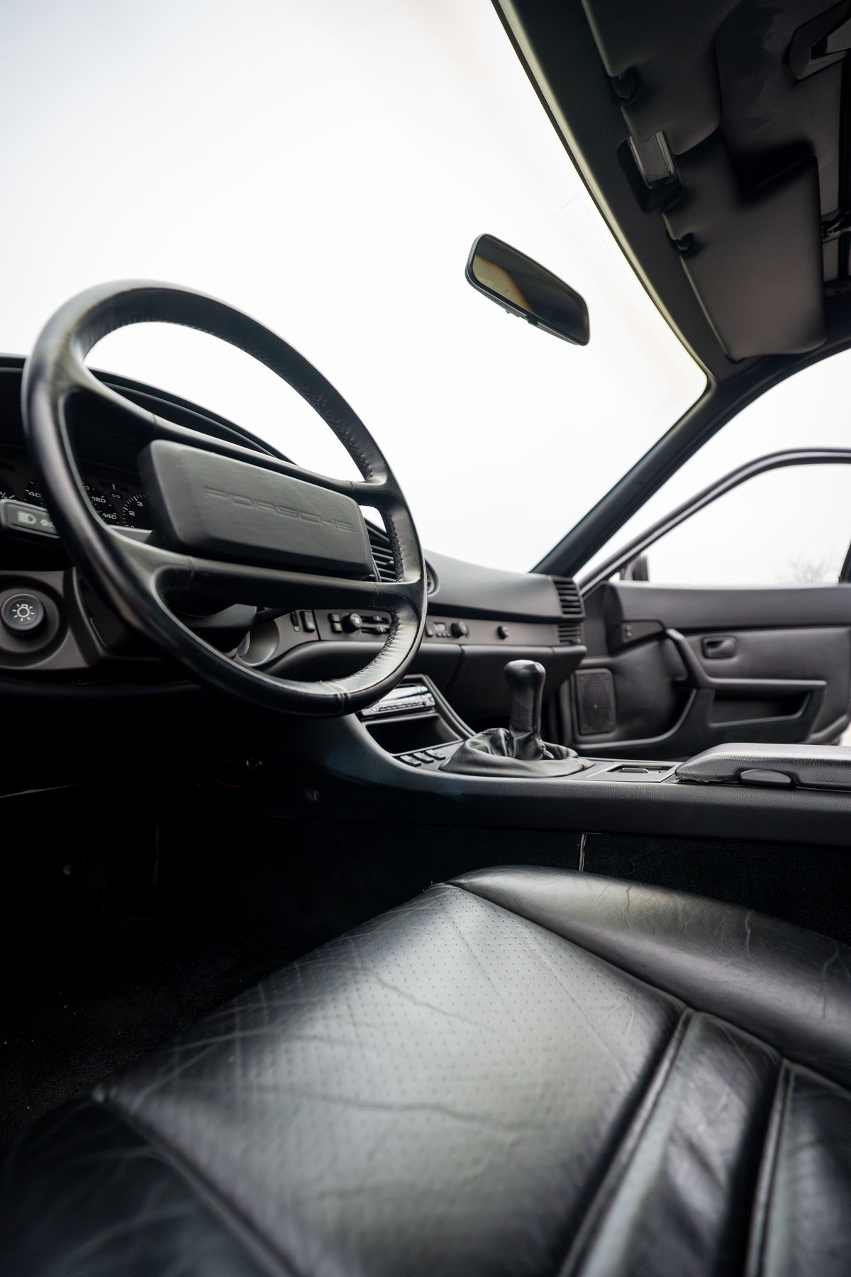 Interior of a black 1986 Porsche 944 Turbo, showing leather seats, steering wheel, and shifter.