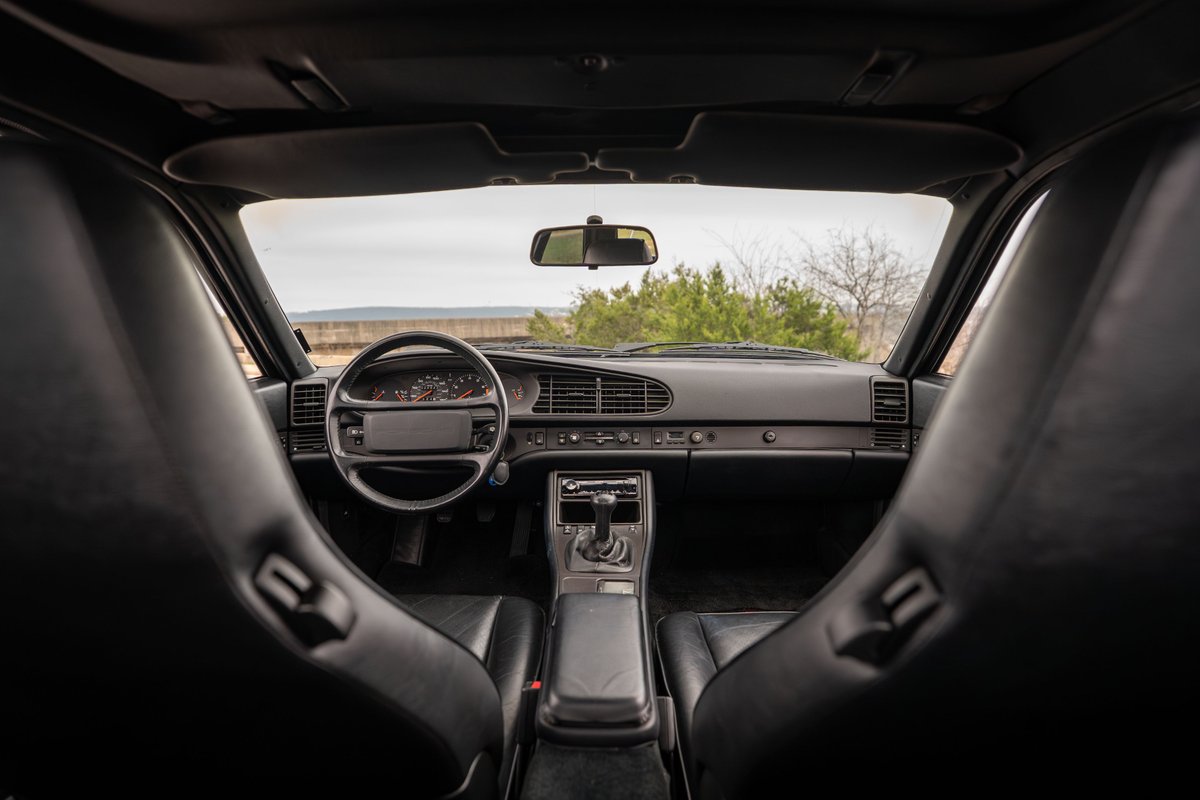 1986 Porsche 944 Turbo interior. Black leather seats and dashboard. View of steering wheel, shifter, and instrument cluster.