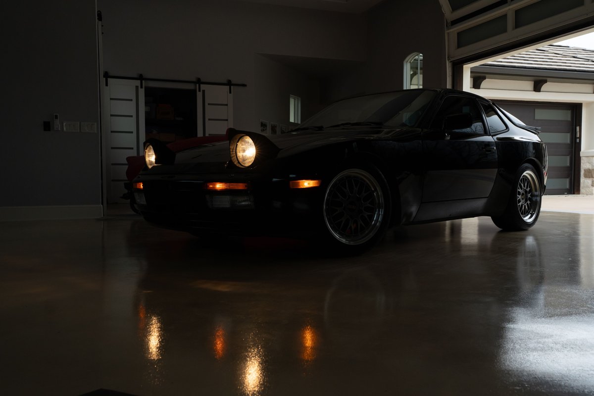 1986 black Porsche 944 Turbo with pop-up headlights and custom rims.