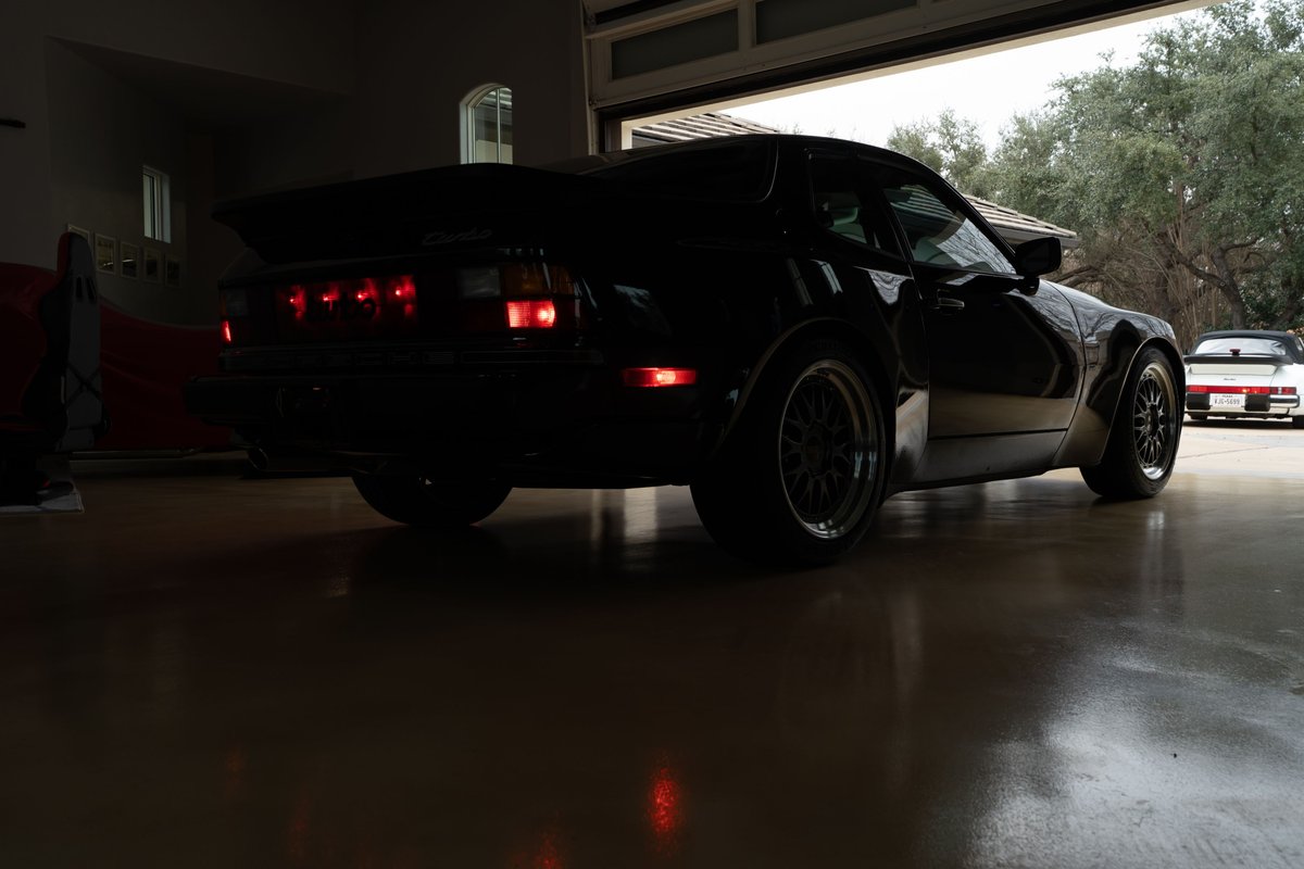 Rear view of a black 1986 Porsche 944 Turbo with aftermarket rims and a large rear spoiler.