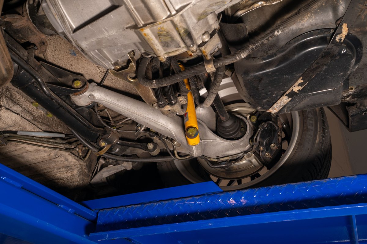 Underbody view of a black 1986 Porsche 944 Turbo, showing suspension, brake caliper, and wheel rim.