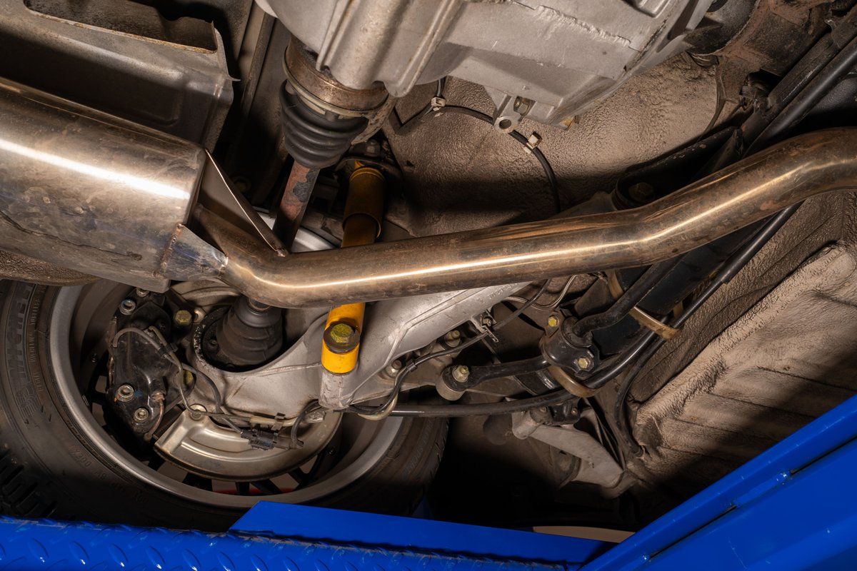 Underneath view of a black 1986 Porsche 944 Turbo showing rear suspension, exhaust, and wheel.