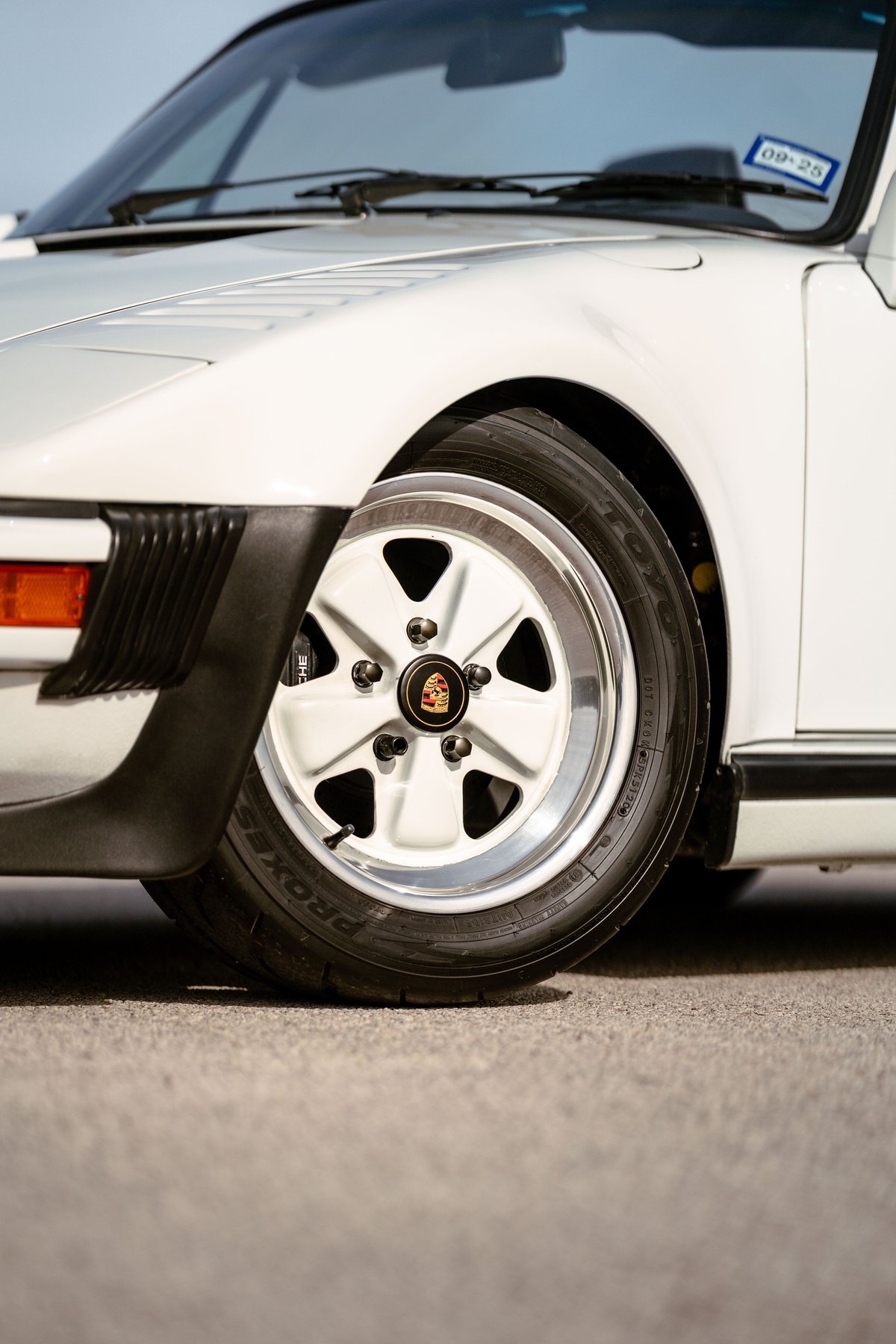 White 1988 Porsche 930 Turbo Slantnose front wheel with a Fuchs rim and black trim.