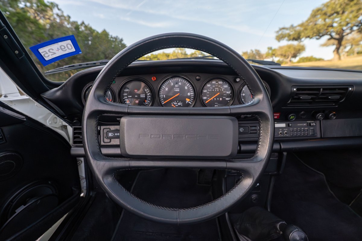 Interior of a white 1988 Porsche 930 Turbo Slantnose showing the steering wheel, dashboard, and gauges.