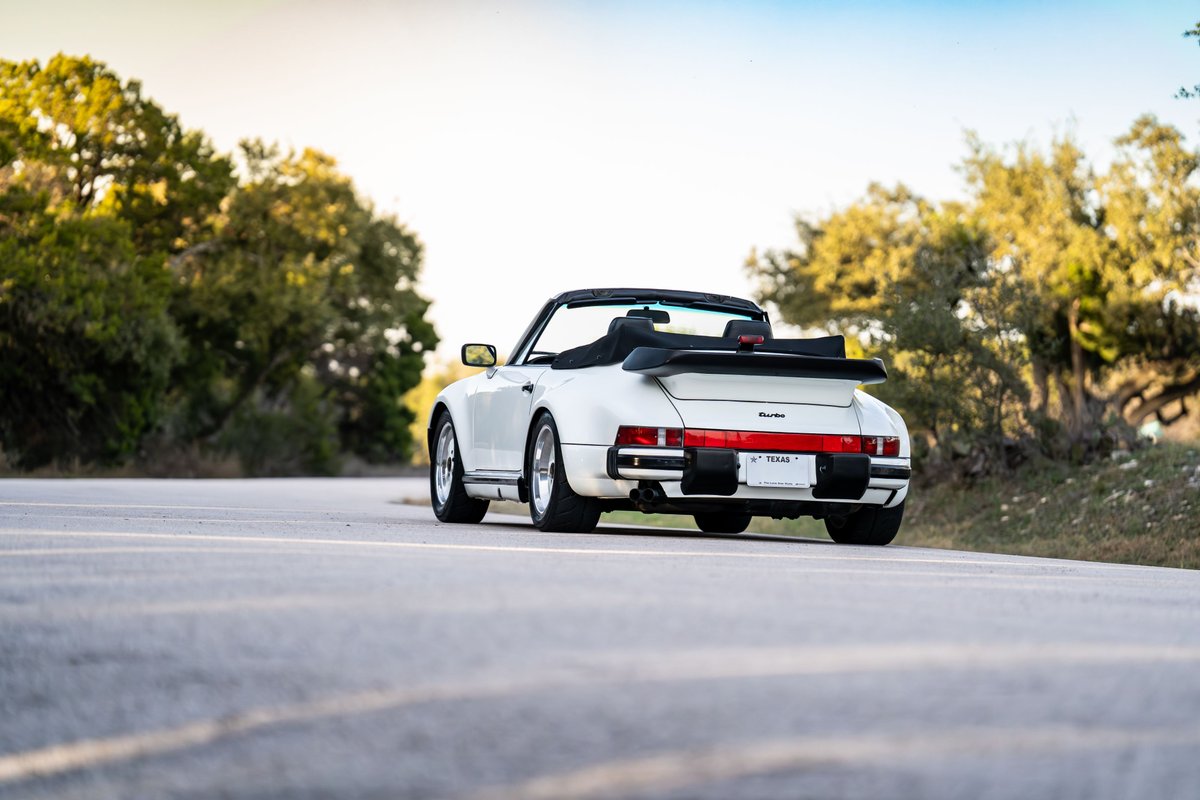 Rear view of a white 1988 Porsche 930 Turbo M505 Slantnose convertible, with classic Fuchs rims and spoiler.
