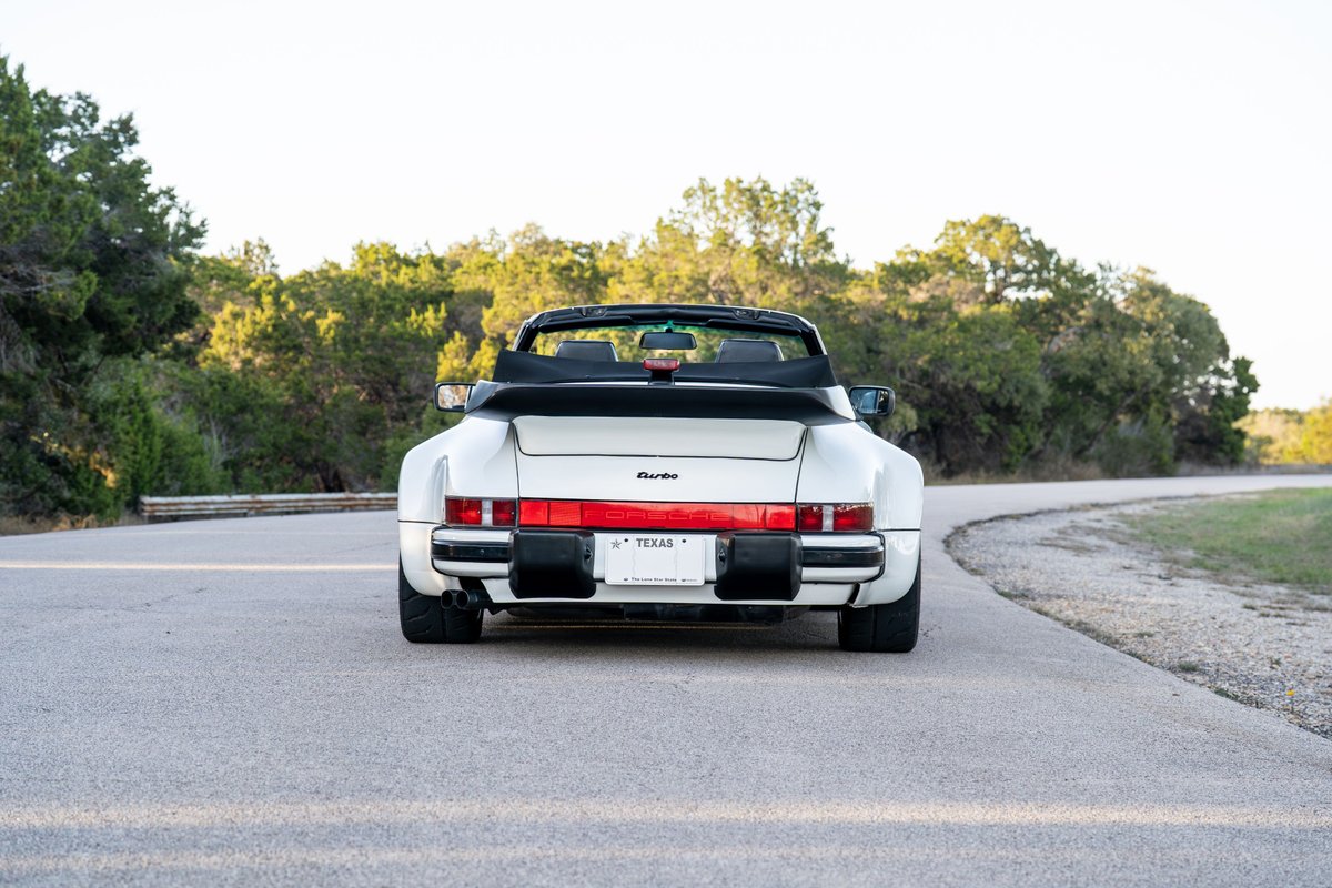 Rear view of a white 1988 Porsche 930 Turbo M505 Slantnose convertible with black trim.