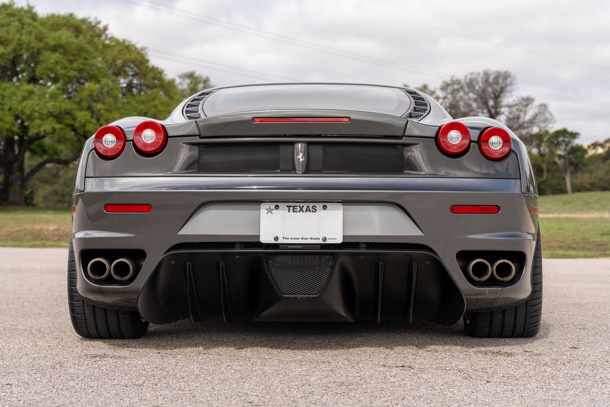 Rear view of a Grigio Silverstone 2007 Ferrari F430 with quad exhaust pipes and red taillights.