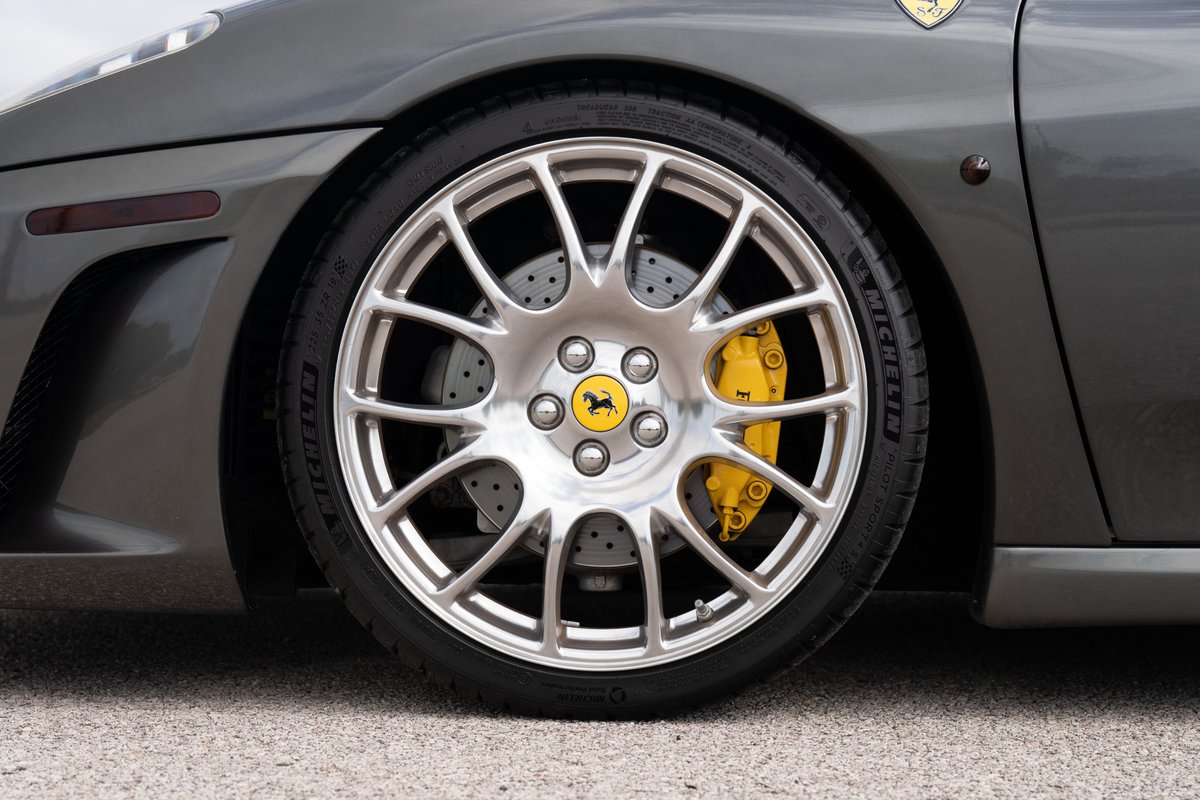 Close-up of a Grigio Silverstone 2007 Ferrari F430 with silver rims and yellow brake calipers.
