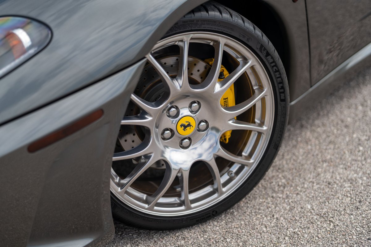 Close-up of a Grigio Silverstone 2007 Ferrari F430's silver multi-spoke rims, yellow brake calipers and Michelin tires.