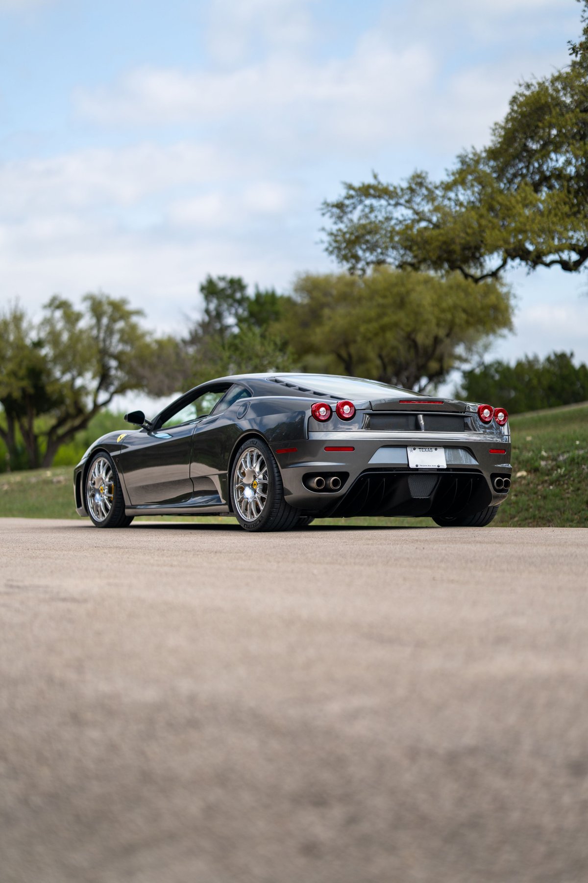 A Grigio Silverstone 2007 Ferrari F430 with chrome multi-spoke rims and quad exhaust pipes.