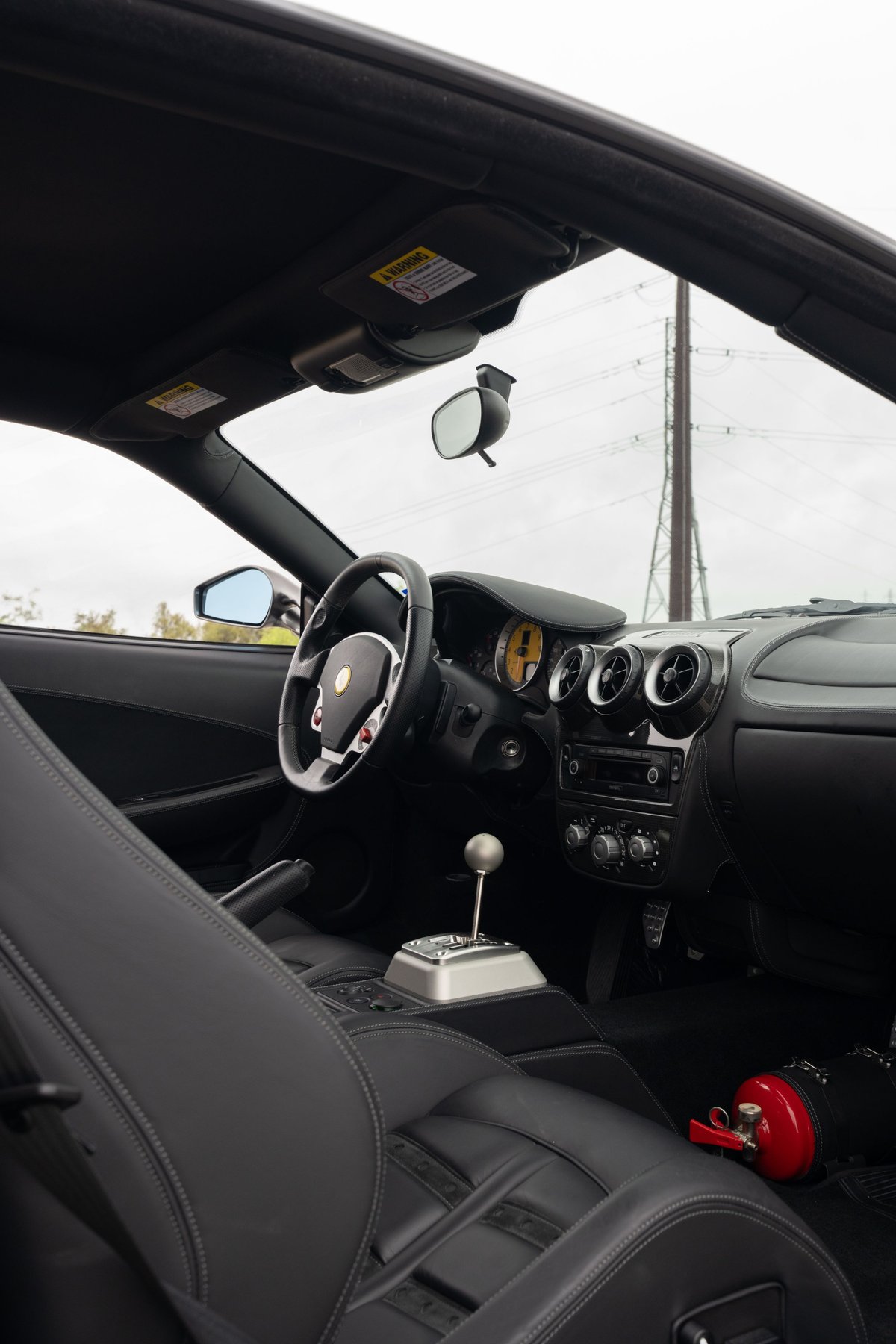 Interior view of a Grigio Silverstone 2007 Ferrari F430 6-speed with black leather seats and silver gated shifter.