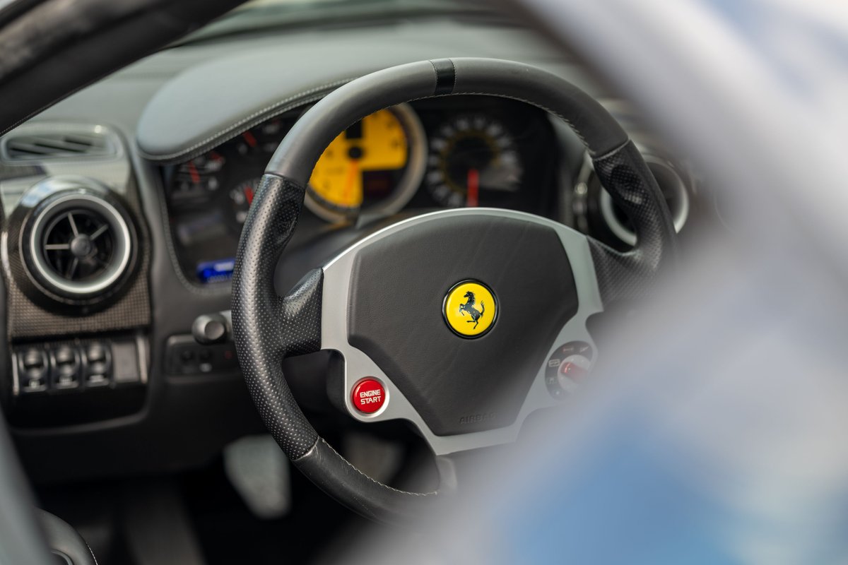 Interior of a 2007 Ferrari F430 in Grigio Silverstone, with a yellow tachometer and red engine start button.