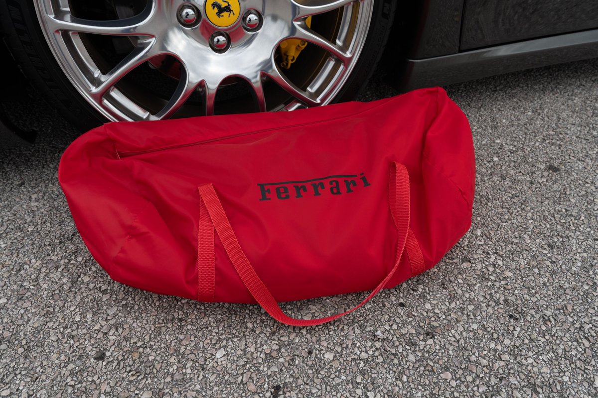 Red Ferrari branded car cover by a silver rim with yellow brake caliper.