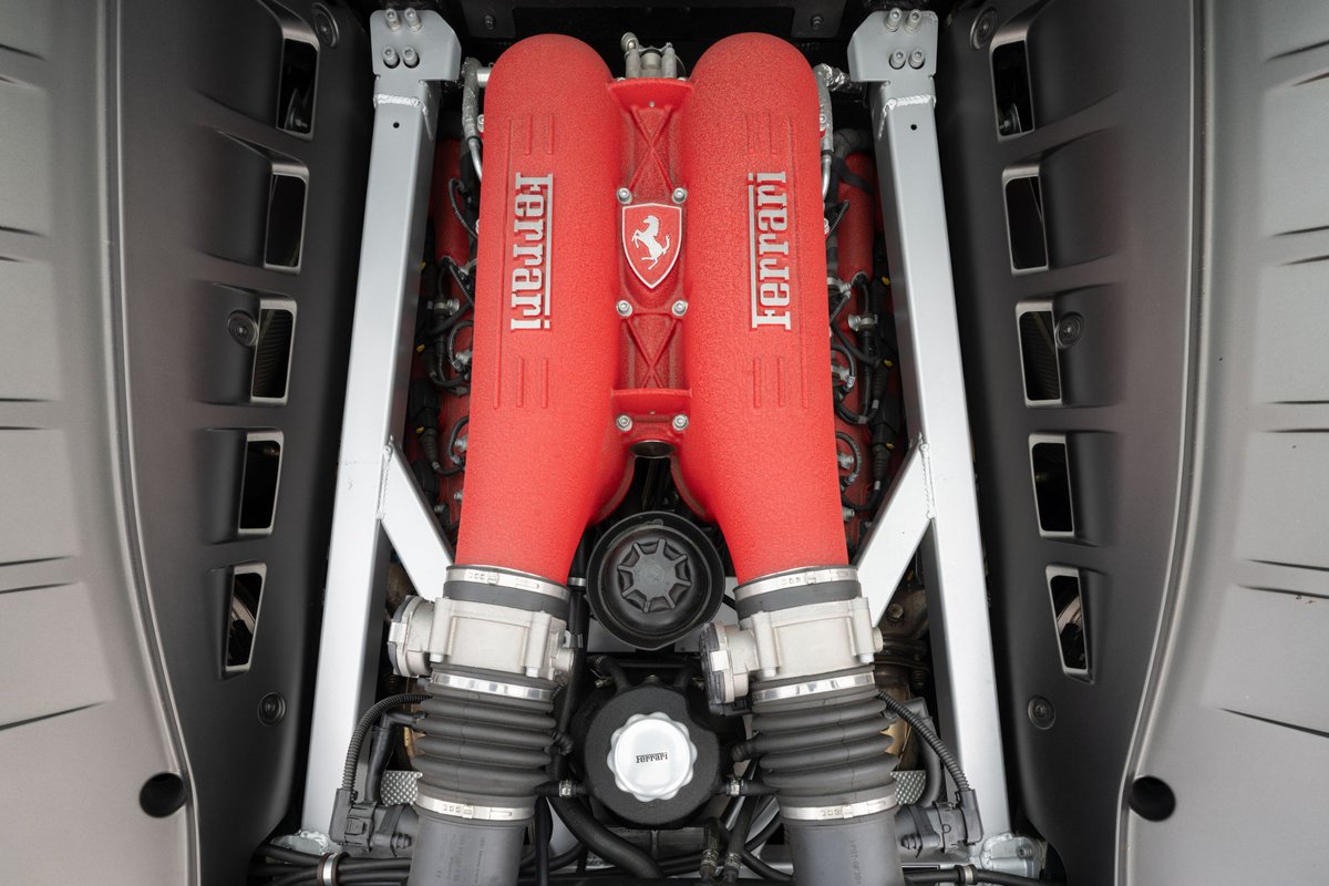 Close-up of the twin red Ferrari intake manifolds and engine bay of a Grigio Silverstone 2007 Ferrari F430.