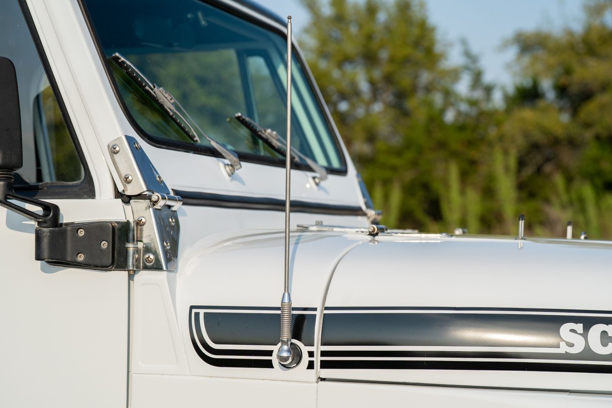 Close-up of a white 1983 Jeep Scrambler with black stripe livery and a chrome antenna.