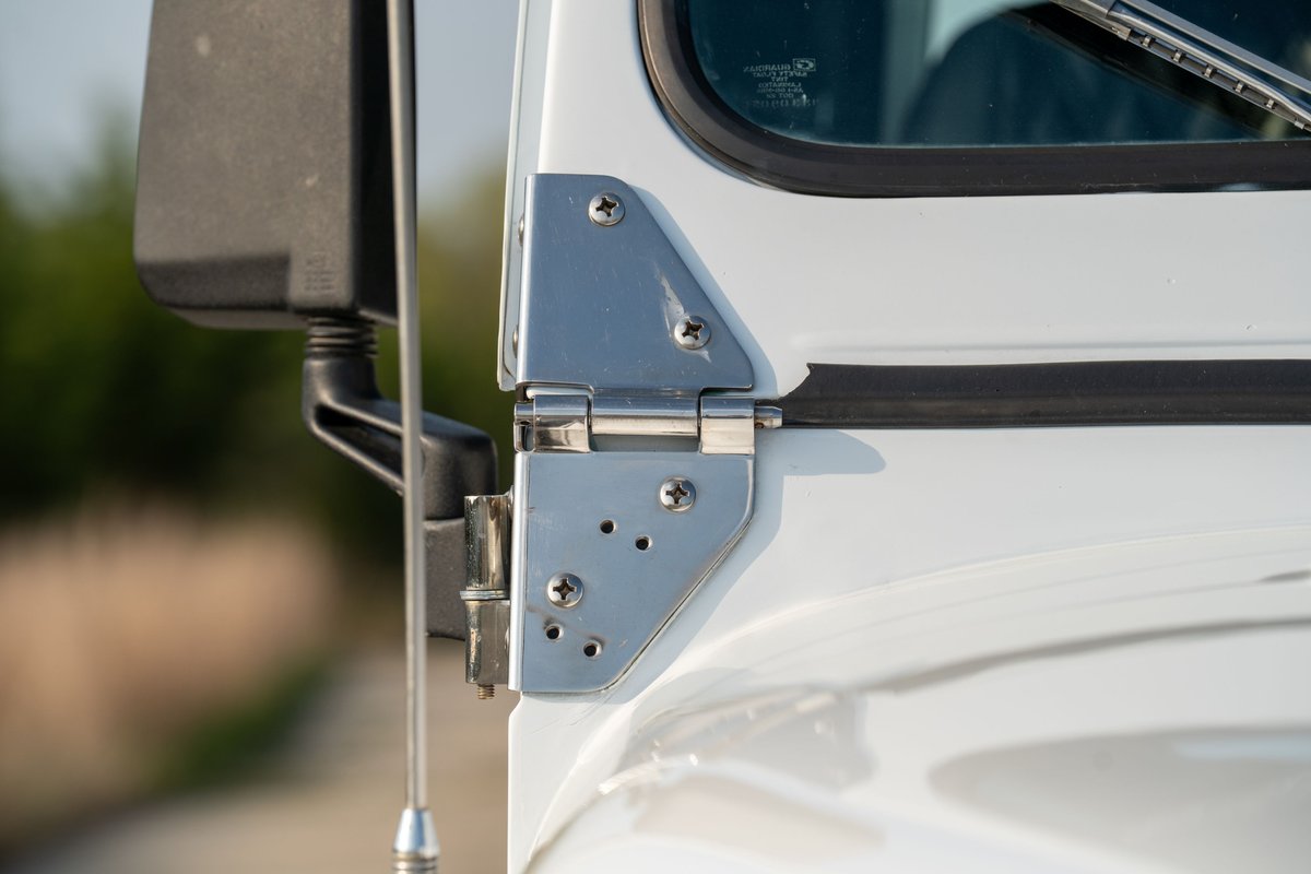 Close-up of a white 1983 Jeep Scrambler door hinge and side mirror mount.