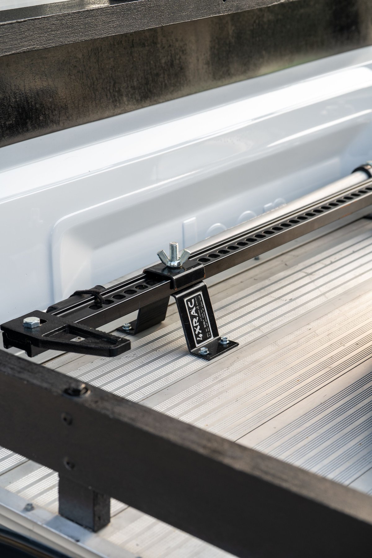Black hi-lift jack mount secured to the aluminum truck bed floor of a white 1983 Jeep Scrambler.