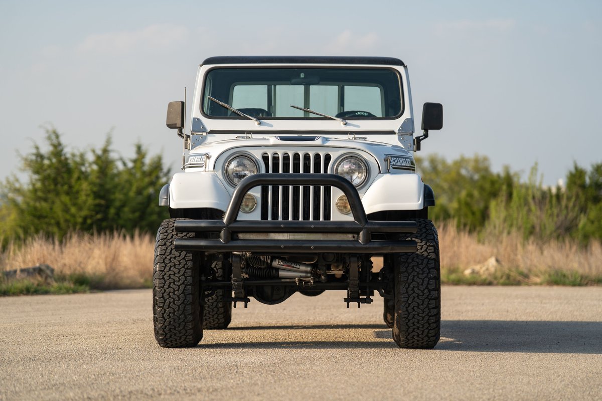 Front view of a white 1983 Jeep Scrambler with a black brush guard, black rims, and off-road tires.