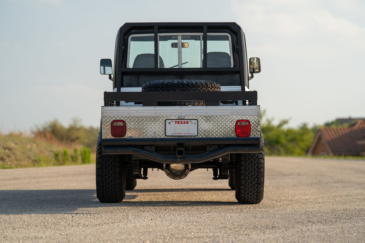 Rear view of a white 1983 Jeep Scrambler with diamond plate bed and spare tire.