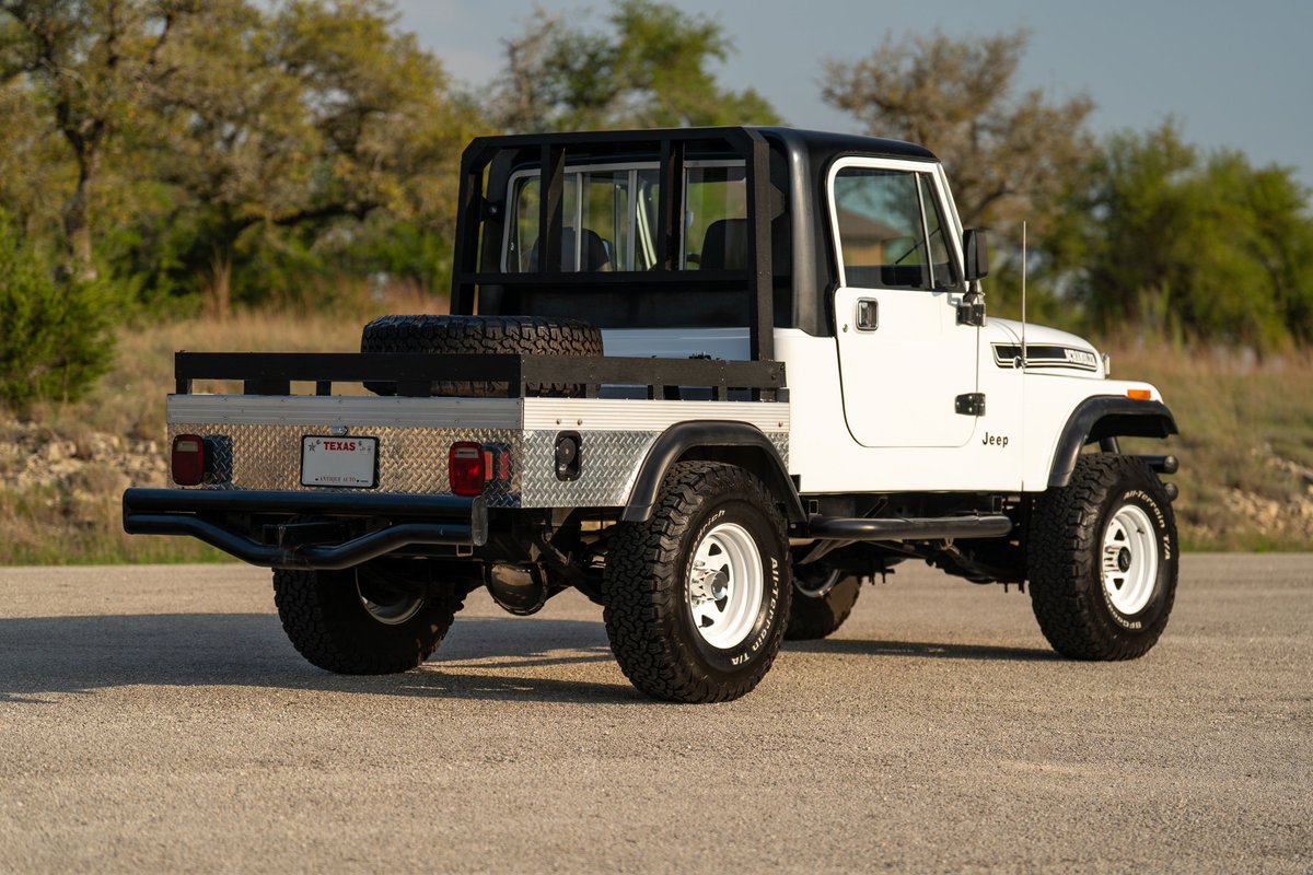 1983 Jeep Scrambler CJ-8 flatbed truck in white with black roll cage and white rims.