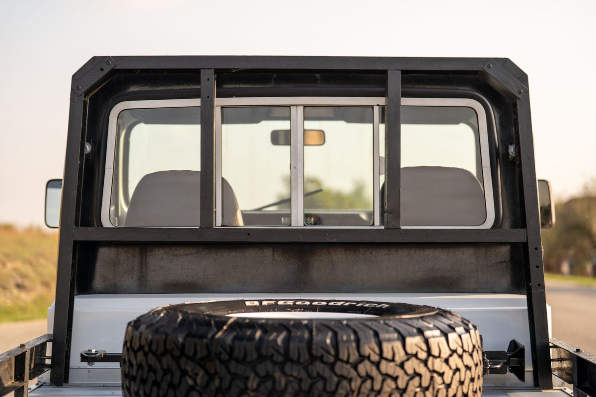 1983 white Jeep Scrambler rear view with spare tire in bed and roll cage.