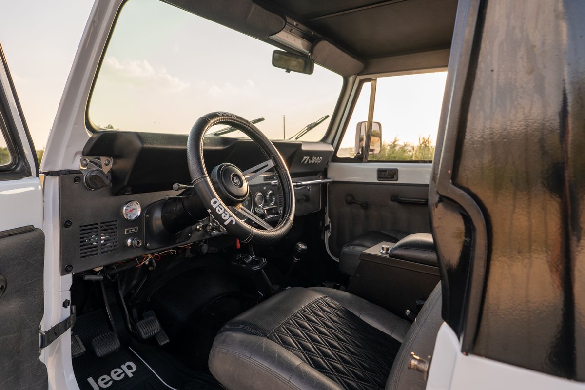 1983 white Jeep Scrambler CJ-8 interior, featuring a Jeep-branded steering wheel and diamond-stitched seats.