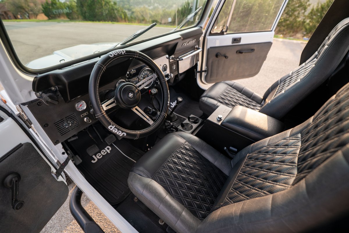 Interior view of a white 1983 Jeep Scrambler with diamond-stitched black leather seats and floor mats.